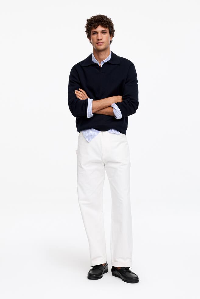 Un pull polo à manches longues bleu marine est superposé à une chemise à col rayée bleu clair et blanche. Il est associé à un pantalon droit blanc et des chaussures bateau à lacets noires, présenté en vue de face complète. - 1