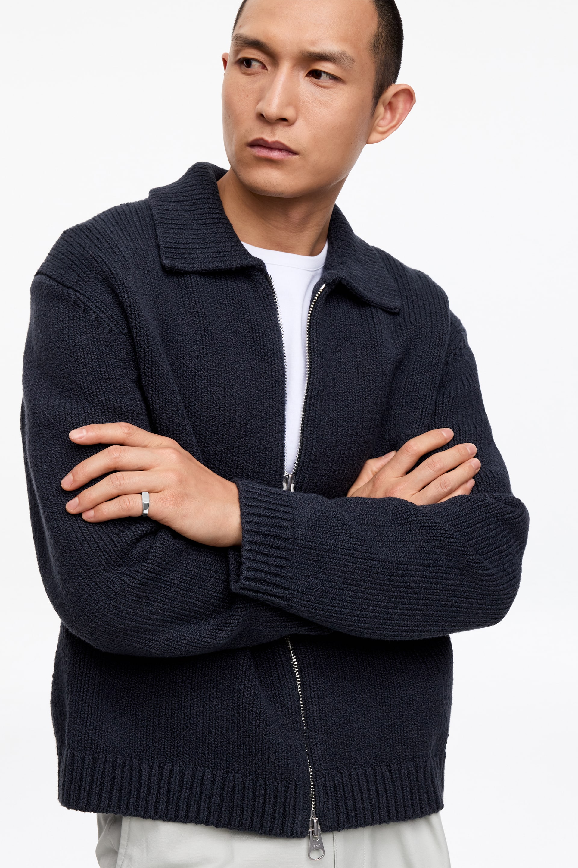 Größeres Bild anzeigen: Ein dunkelblauer, strukturierter Strickcardigan wird präsentiert, mit aufgeschlagenem Kragen, durchgehendem Reißverschluss und Rippstrickbündchen an Ärmeln und Saum. Er wird offen über einem weißen T-Shirt getragen.