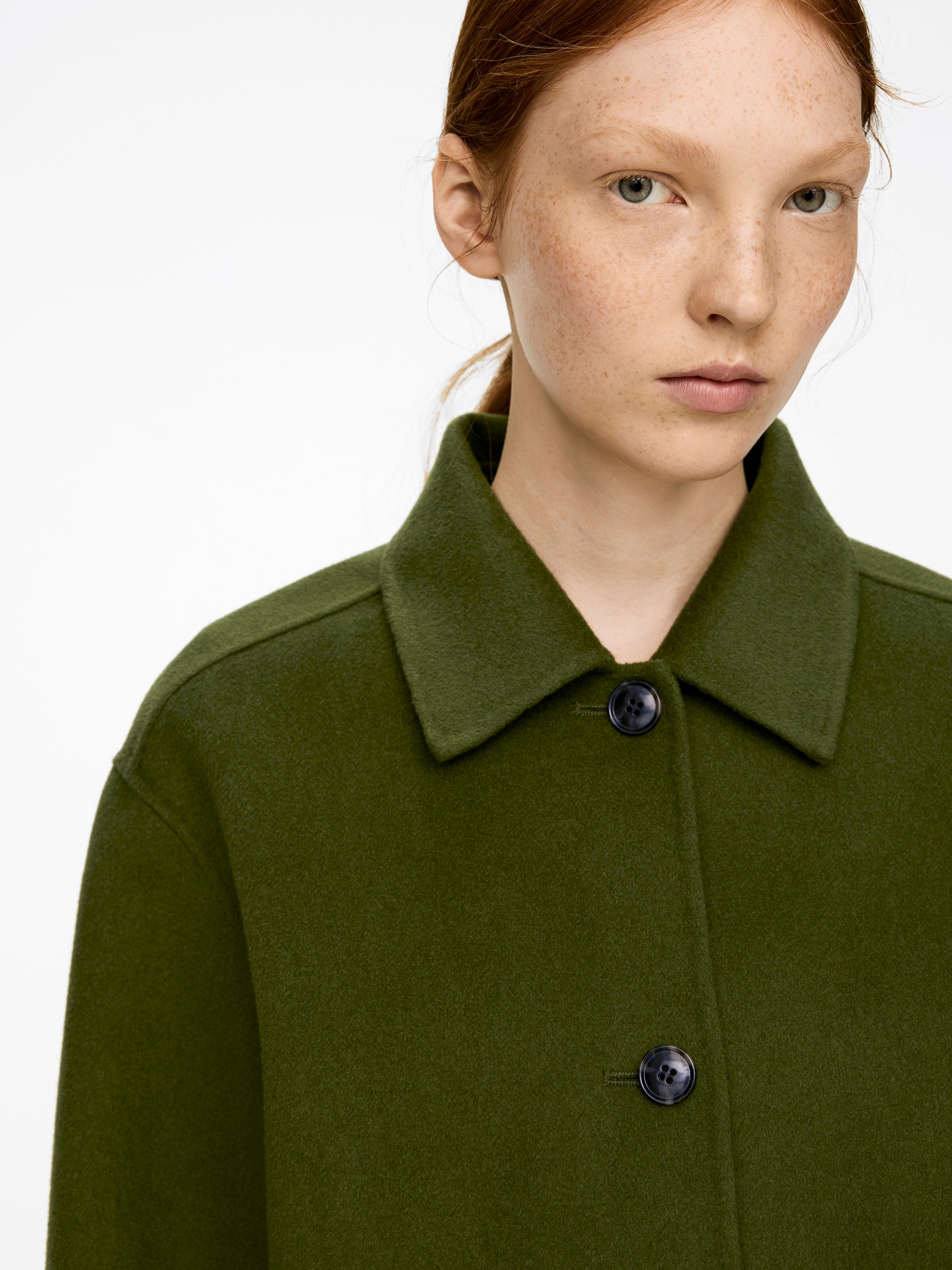 Ver imagen más grande: Una sobrecamisa verde oliva está siendo usada por el modelo. Presenta un escote con cuello y un cierre frontal con botones oscuros, confeccionada con un tejido de mezcla de lana texturizada.