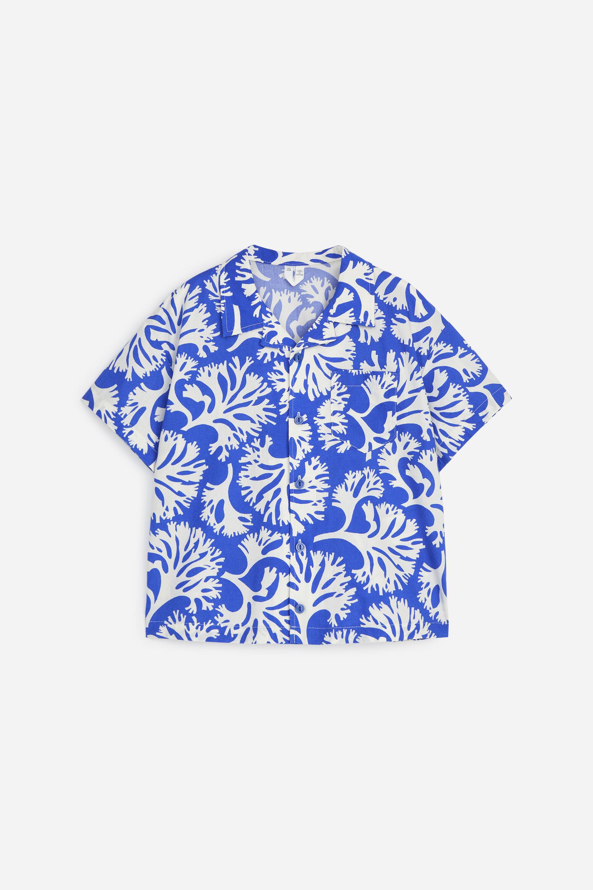 Agrandir l'image: La chemise à manches courtes présente un fond bleu avec un motif blanc semblable à du corail, dotée d'un col cubain. Elle arbore une fermeture boutonnée avec des boutons blancs visibles et une poche plaquée unique sur la poitrine gauche.