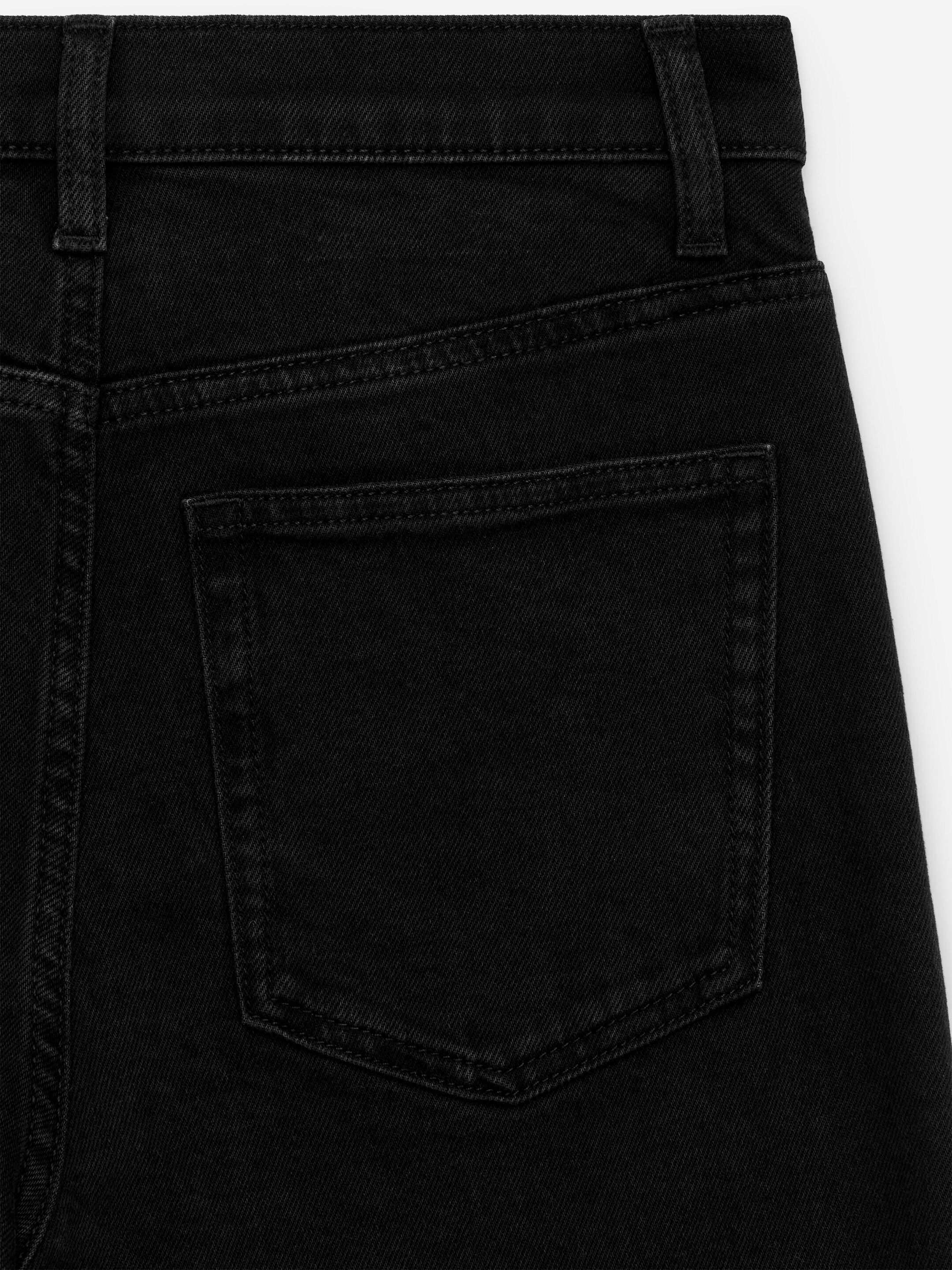 Größeres Bild ansehen: Schwarze Jeans aus Denim werden von hinten präsentiert, mit einem Bund mit Gürtelschlaufen und einer einzelnen aufgesetzten Tasche auf der rechten Seite. Schwarze Nähte verzieren die Tasche und die Nähte auf dem schwarzen Denimstoff.