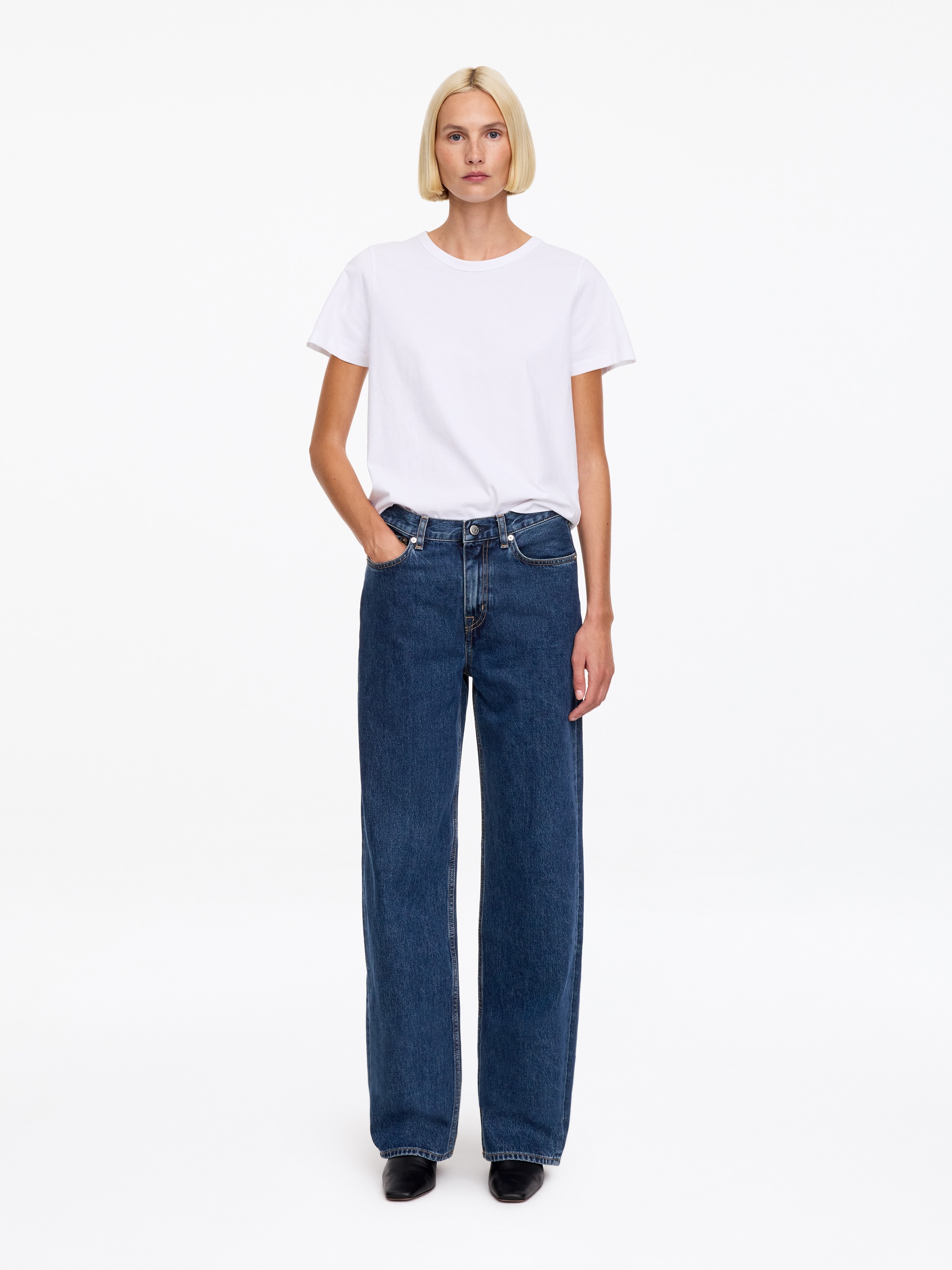 Un paio di jeans in denim blu Ã¨ mostrato frontalmente, con vita alta, classico design a cinque tasche e una silhouette ampia e rilassata. I jeans presentano cuciture a contrasto arancioni, passanti per la cintura e chiusura centrale con bottone in vita.