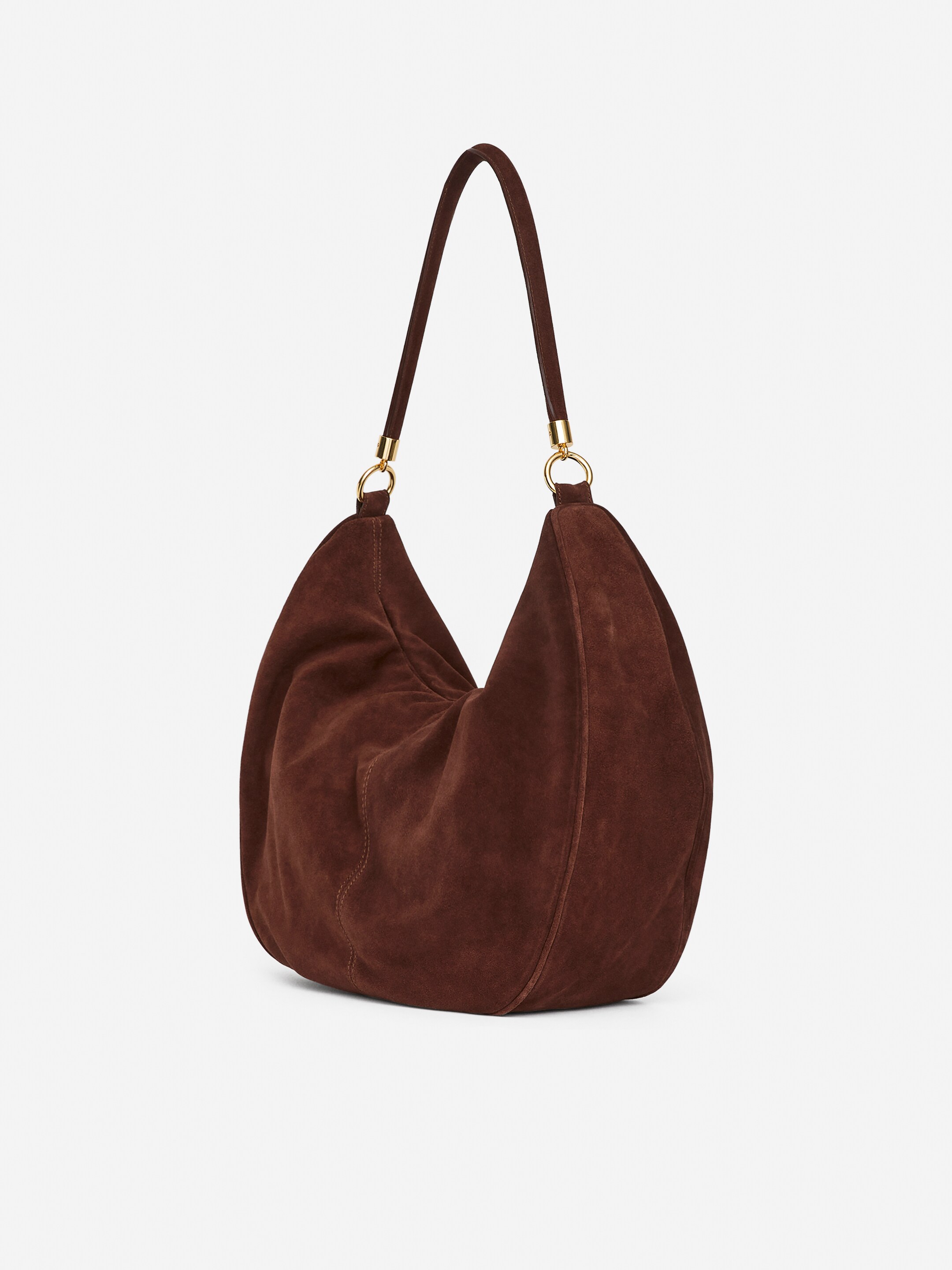 Grösseres Bild ansehen: Eine braune Wildleder-Schultertasche ist schräg gestellt und zeigt ihre weiche, lässige Form. Sie verfügt über einen einzelnen Schulterriemen, der durch goldfarbene Ringe verbunden ist.