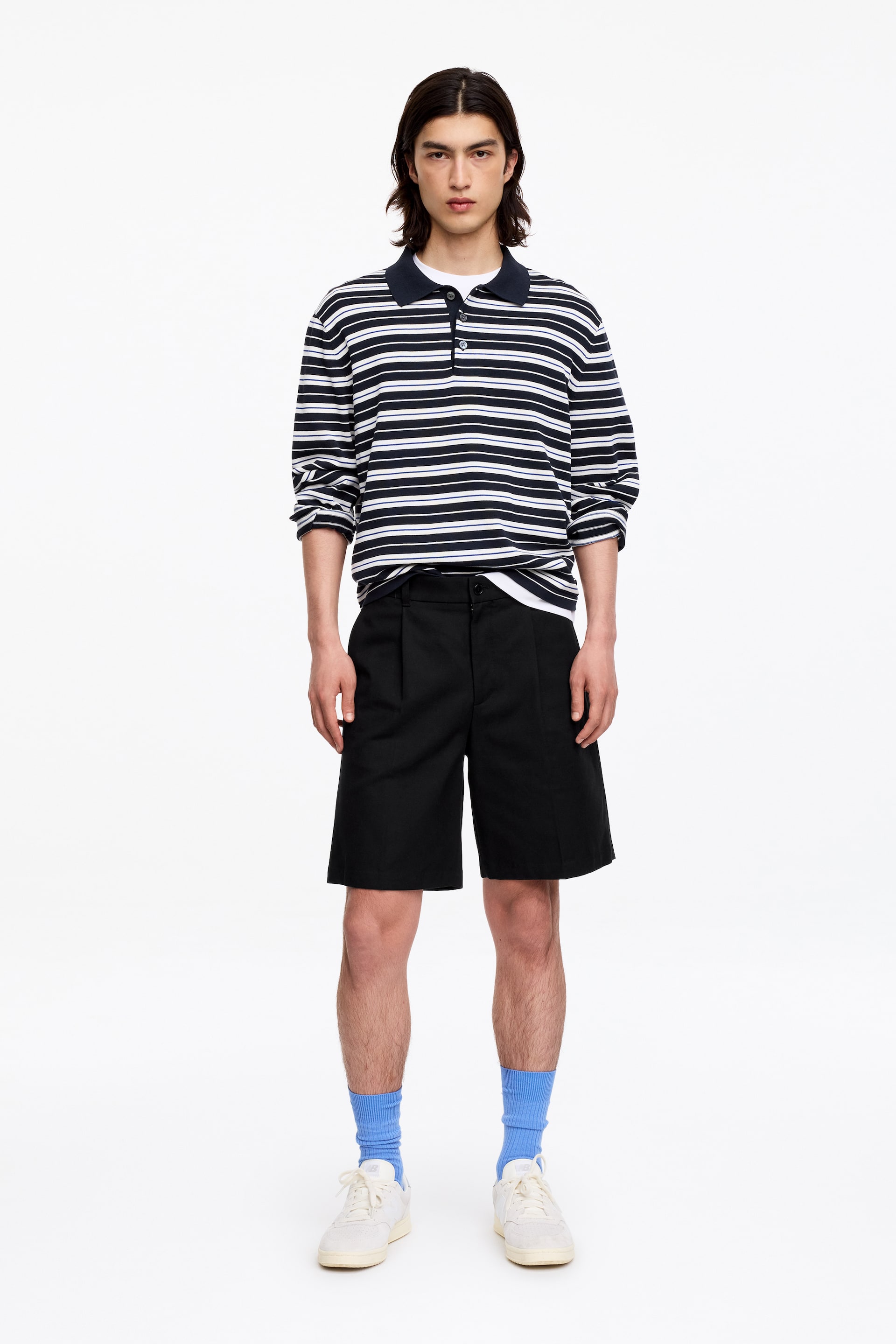 Grotere afbeelding bekijken: Een poloshirt met lange mouwen toont een patroon van marineblauwe en witte strepen met dunne rode en blauwe accentlijnen. Het heeft een effen marineblauwe kraag, een drieknoopssluiting en wordt gedragen over een wit t-shirt, wat een ontspannen pasvorm presenteert.