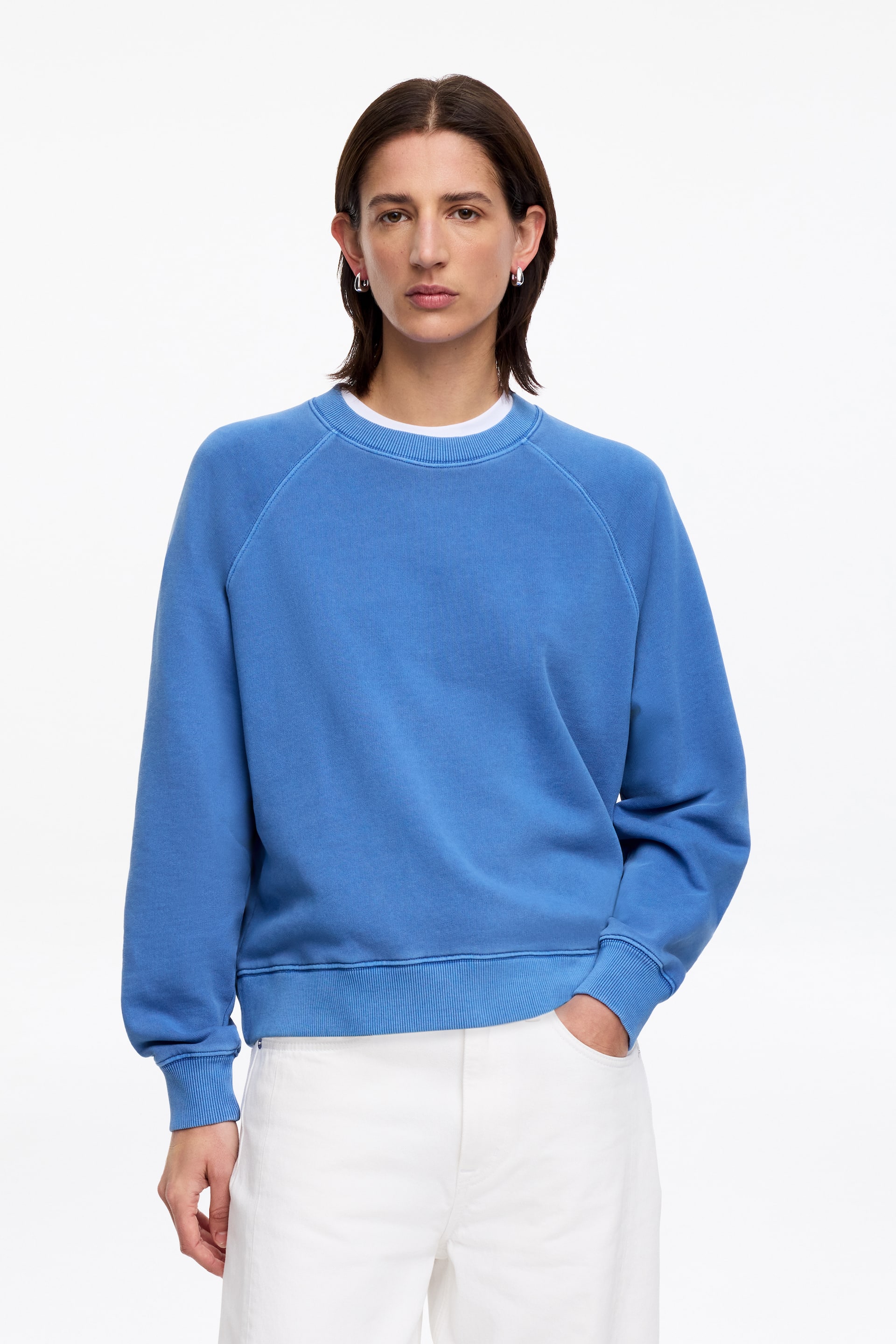 Grösseres Bild ansehen: Ein blauer Sweatshirt mit Rundhalsausschnitt, Raglanärmeln, gerippten Bündchen und geripptem Saum, darunter ein weißes T-Shirt, das am Halsausschnitt sichtbar ist.