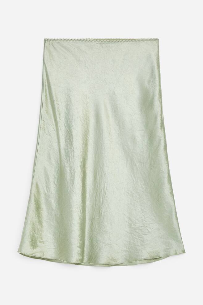 A light green slip skirt featuring a crinkled satin-effect material, with its front side facing forward. It showcases a serged top edge and a simple hem. - 1