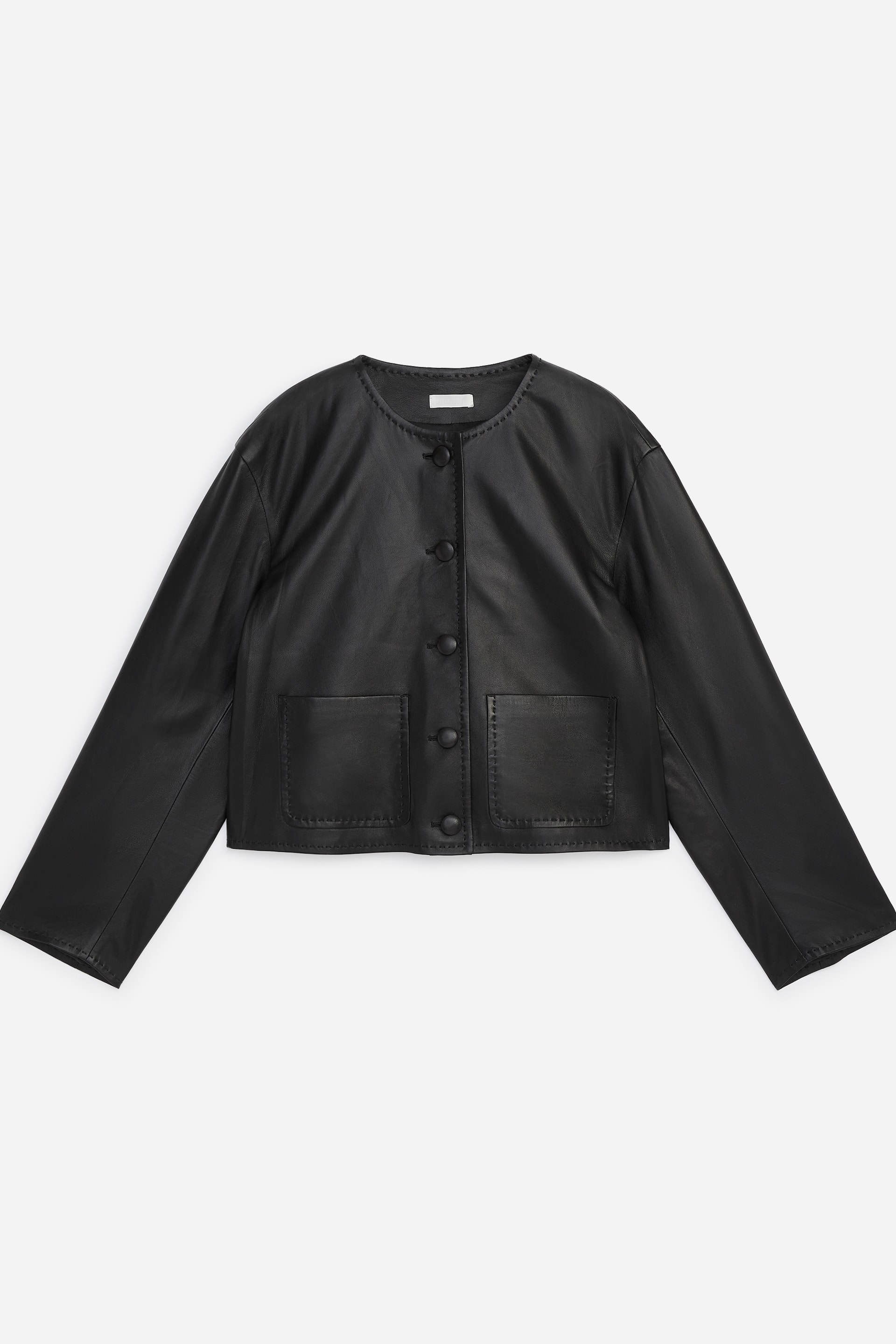 Ver imagen más grande: Una chaqueta de cuero negra está de frente, con un diseño sin cuello y un escote con borde perforado. Presenta un cierre frontal de cuatro botones. Se pueden ver dos bolsillos de parche en la parte inferior delantera, cada uno detallado con costuras decorativas, que también delinean la tapeta frontal y el escote.