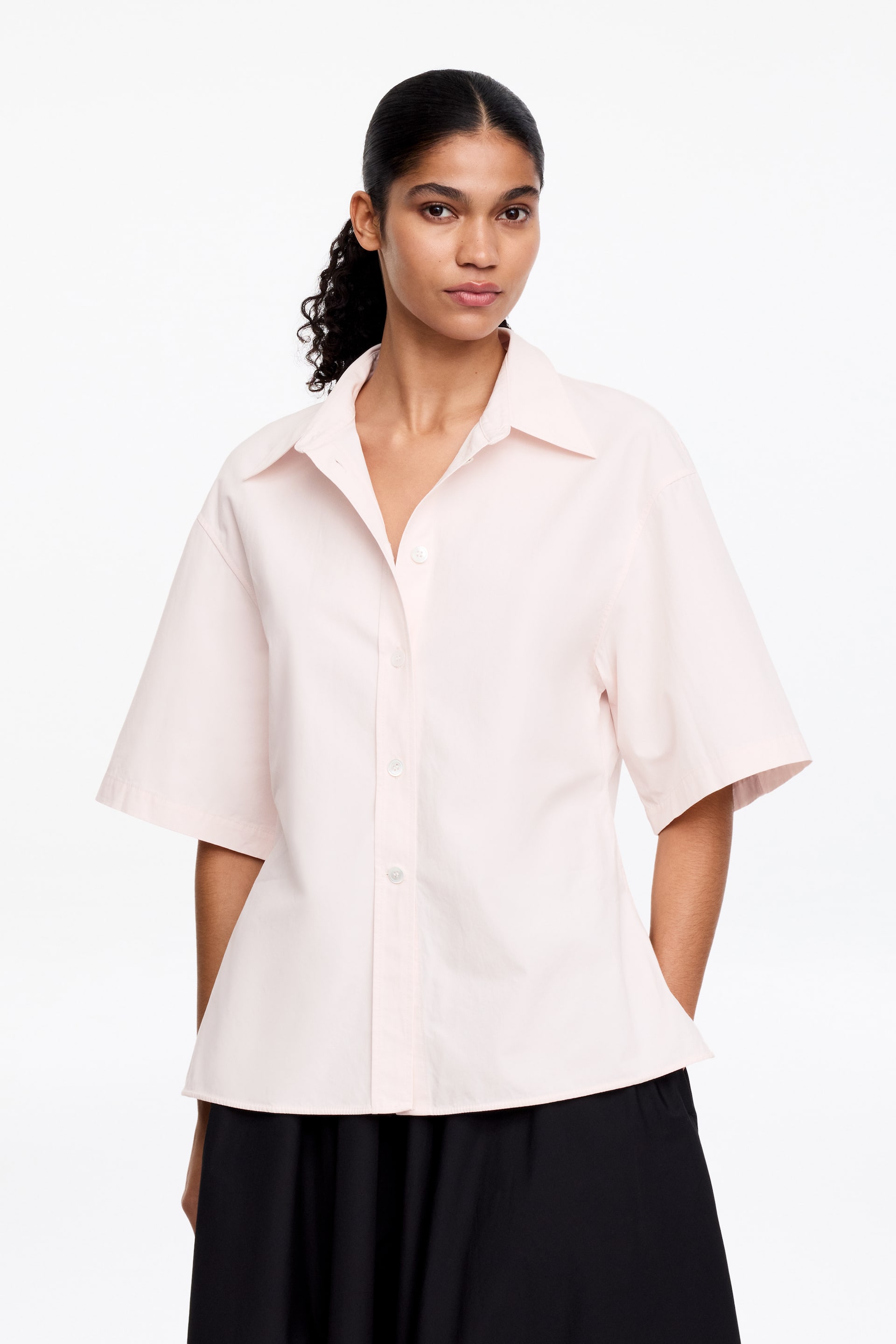 Ver imagen más grande: Una camisa de manga corta rosa claro presenta un corte holgado, mangas cortas anchas, un cuello abierto y una botonadura completa en la parte delantera con botones blancos.