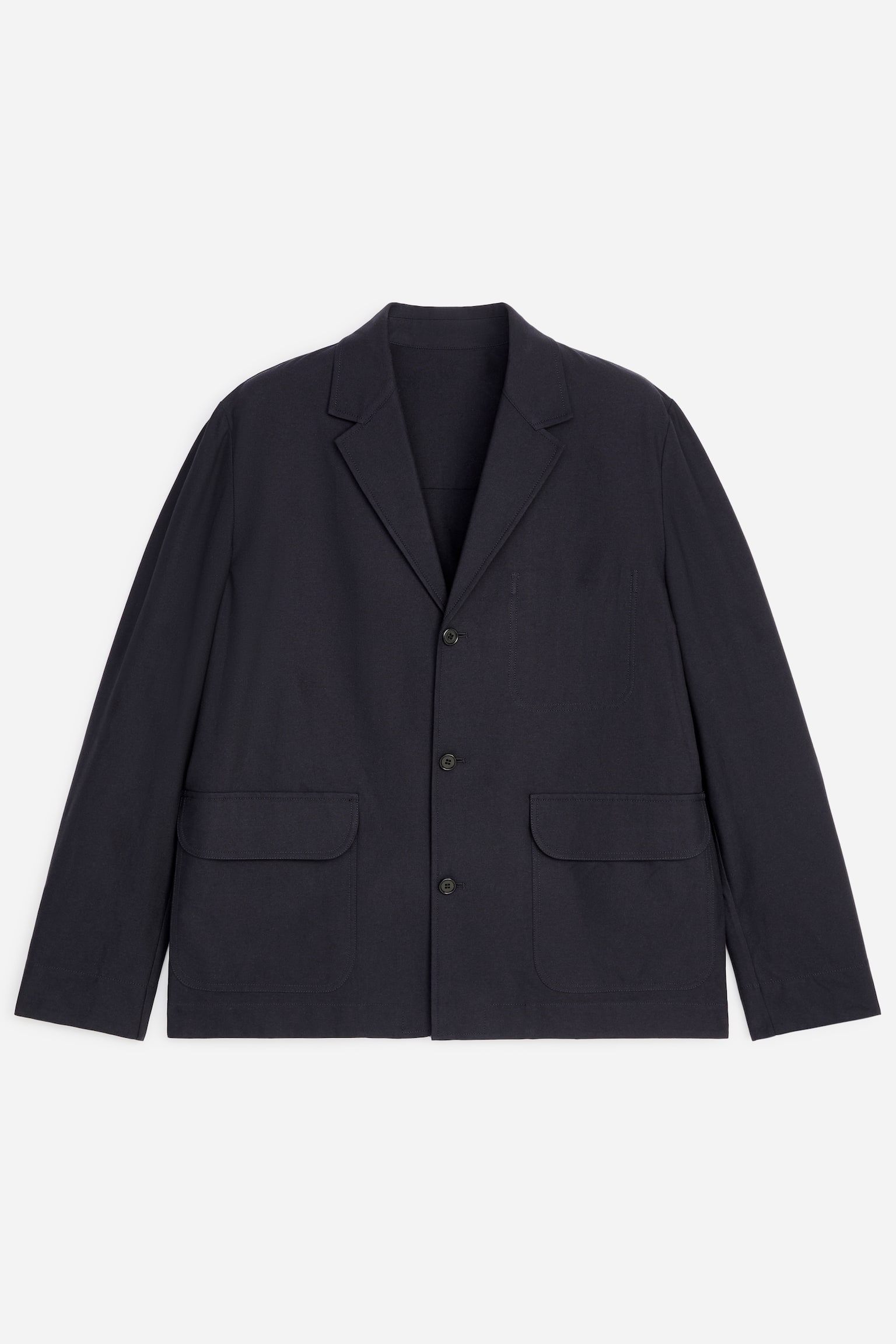 Una giacca blu scuro è mostrata di fronte, con revers a dente e una chiusura frontale a tre bottoni. Presenta due ampie tasche applicate in vita e una tasca applicata più piccola sul petto sinistro.