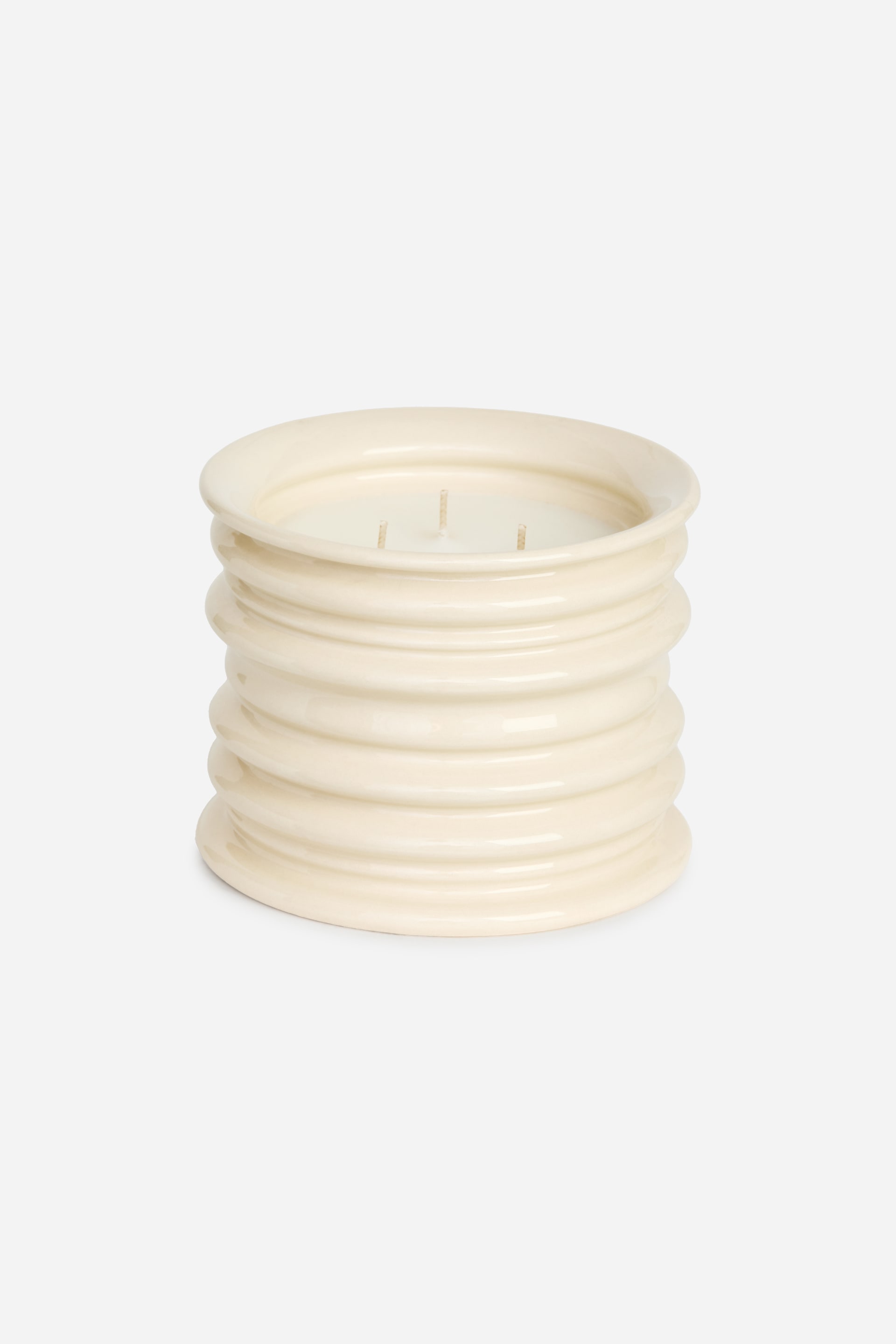 View larger image: A cream-coloured cylindrical candle is shown with a ribbed exterior, viewed from a slightly elevated front angle. It features three wicks in its light-coloured wax.