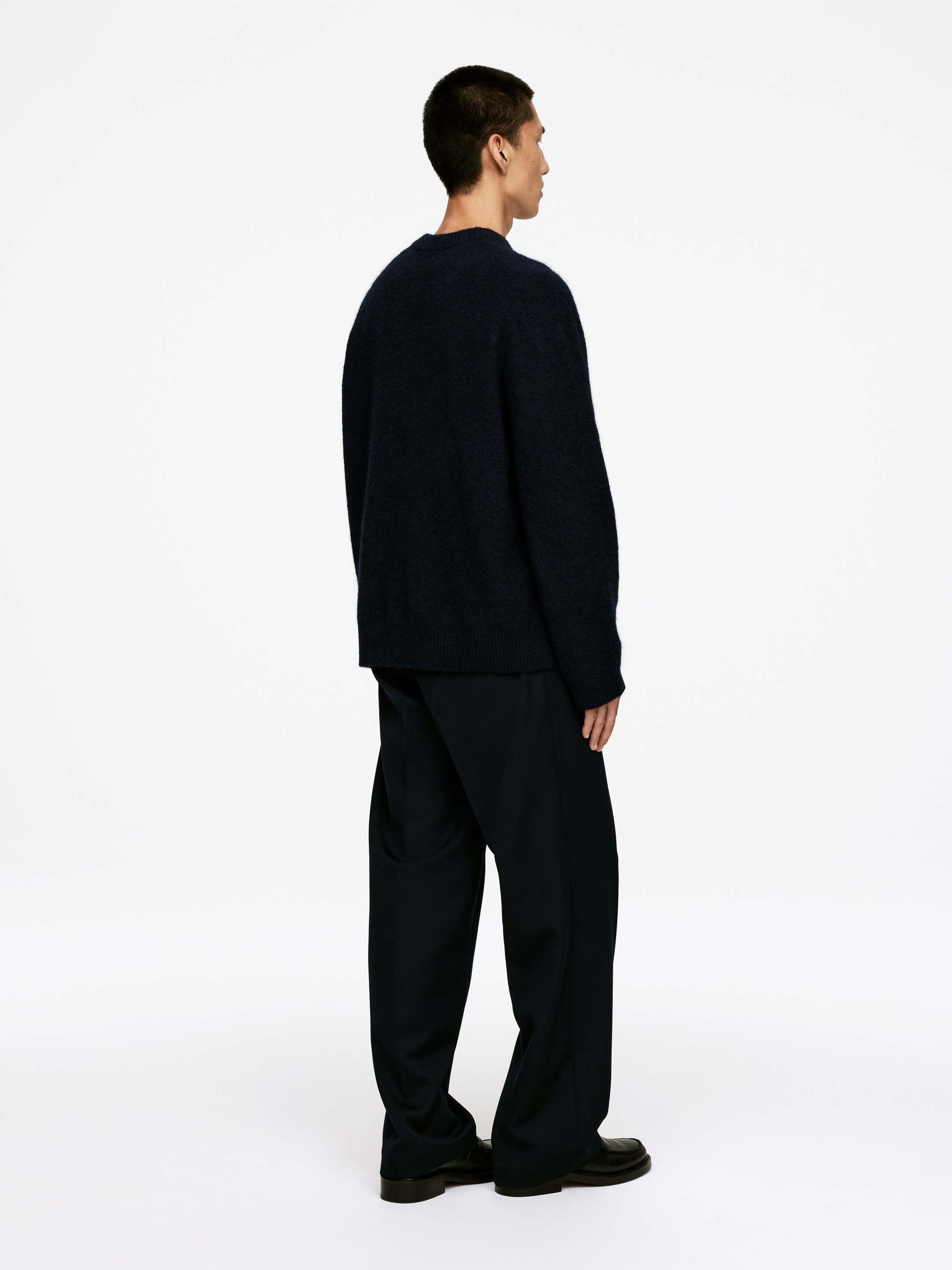 Ingrandisci l'immagine: Un maglione blu scuro con scollo a girocollo e una texture a maglia spazzolata viene indossato, mostrato da dietro e di lato, ed è abbinato a pantaloni neri larghi.