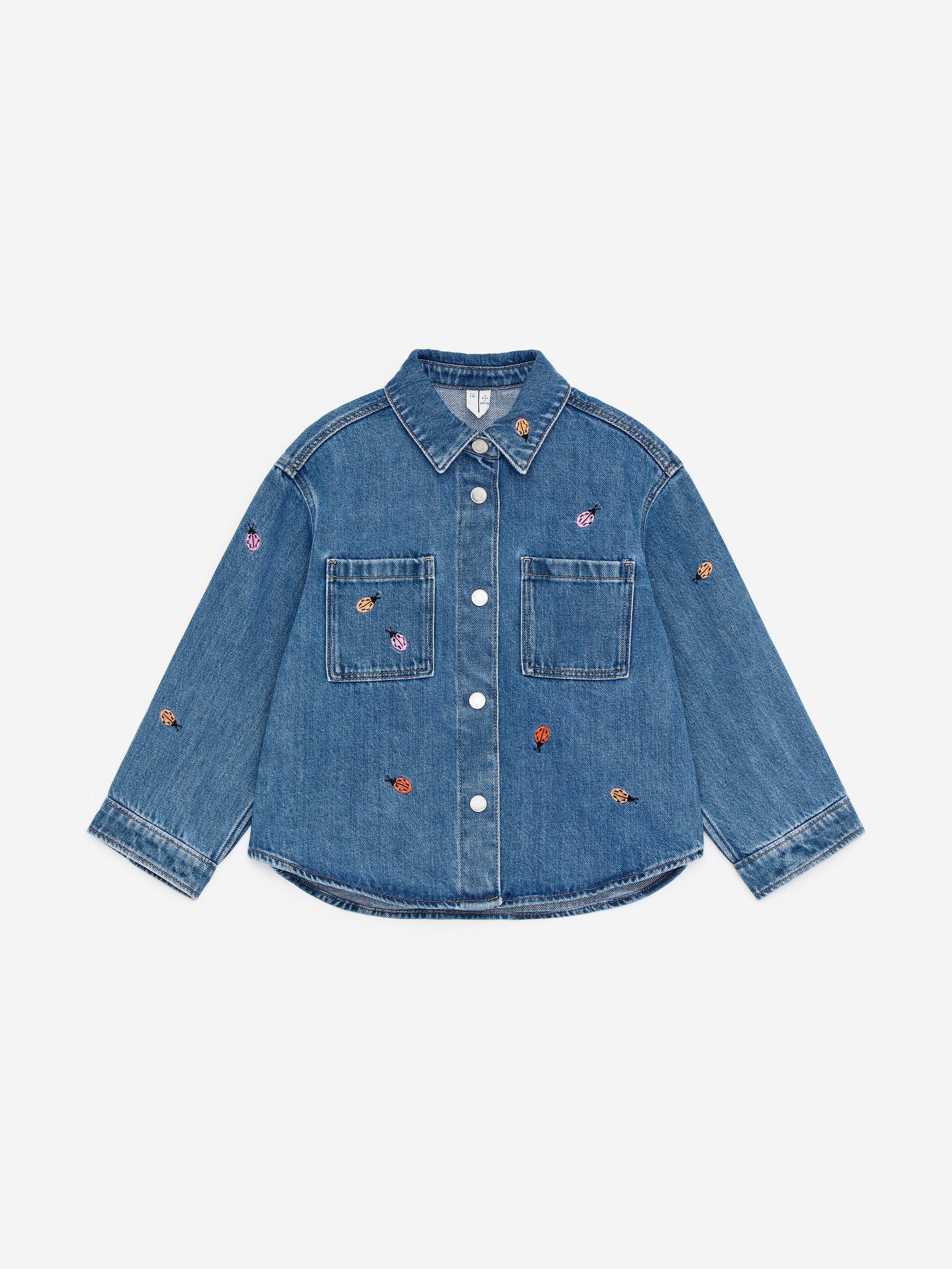 Agrandir l'image: Une chemise en jean est présentée de face, avec des détails brodés sur l’ensemble. Elle affiche une fermeture à pressions sur le devant, deux poches plaquées au niveau de la poitrine et des poignets boutonnés.