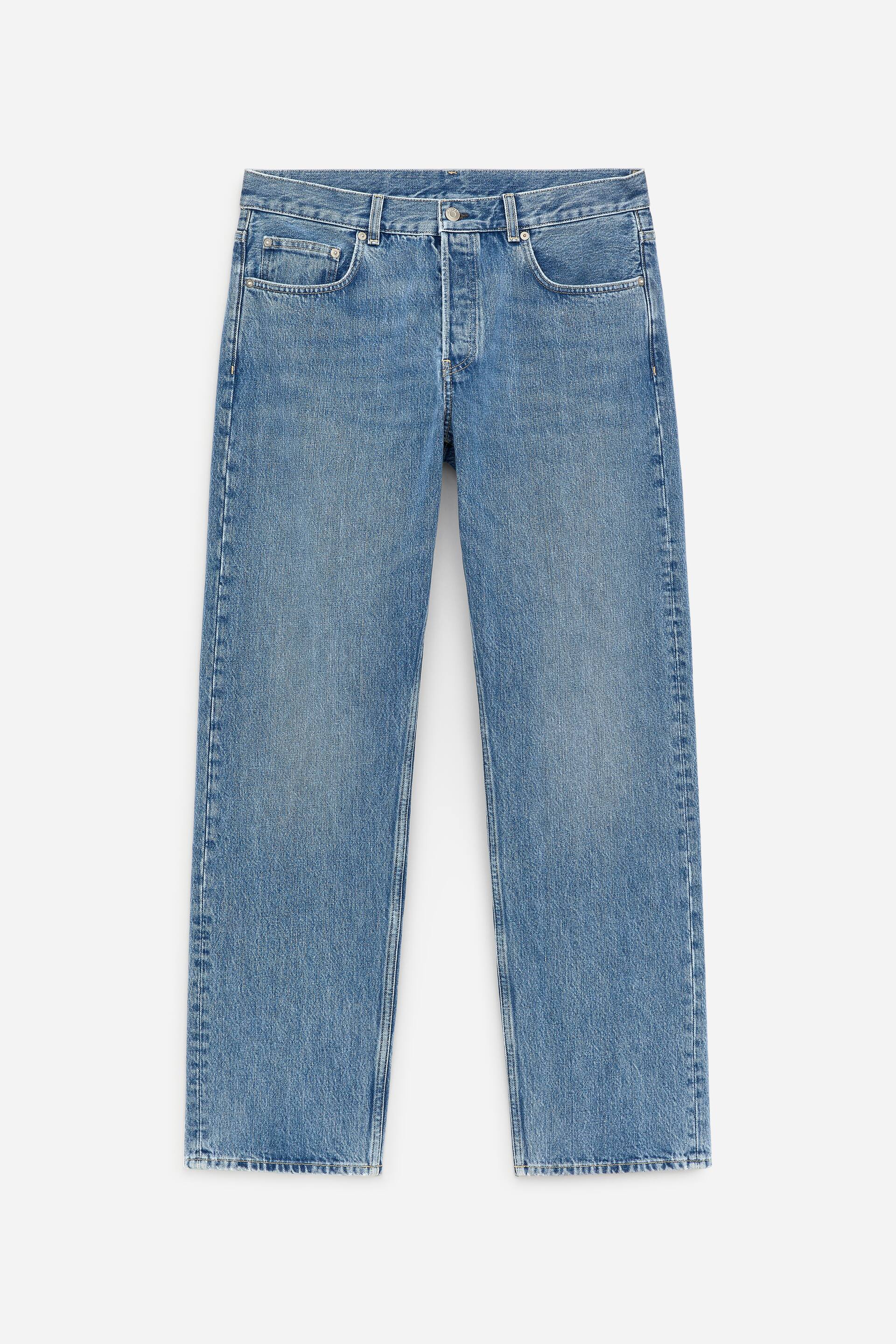 Se større billede: Blå denimjeans præsenteres forfra, med en mellemhøj talje og en knaplukning. De har lige, fuldlange ben, forlommer ved hofterne og en lys vask.