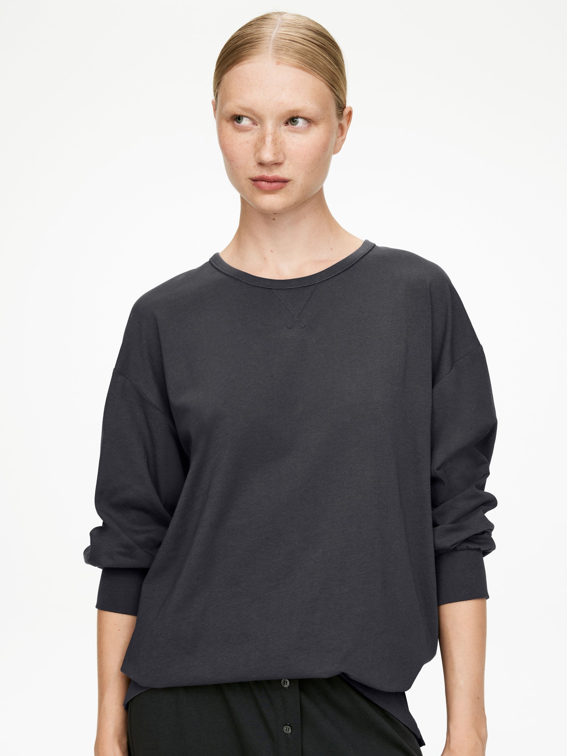 Agrandir l'image: Un sweat-shirt gris foncé est porté, face vers l'avant. Il présente un col rond avec un détail en V en dessous, des manches longues et amples se terminant par des poignets côtelés, et un ourlet droit.