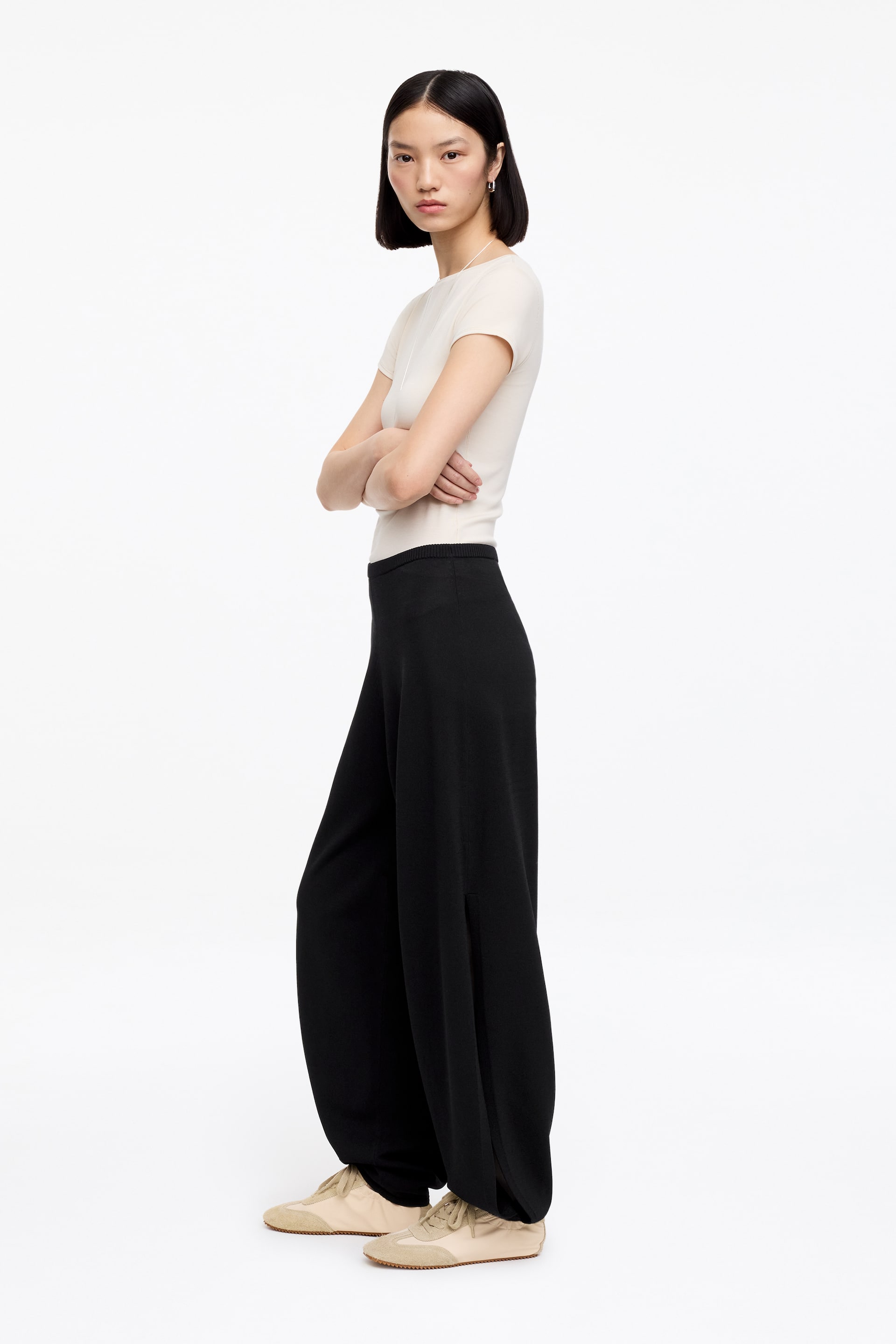 Ver imagen más grande: Pantalones negros de pierna ancha que presentan un ajuste de talle alto y una silueta fluida, con una abertura lateral larga visible en la parte exterior de la pierna. Caen sobre los zapatos, vistos desde un ángulo lateral.