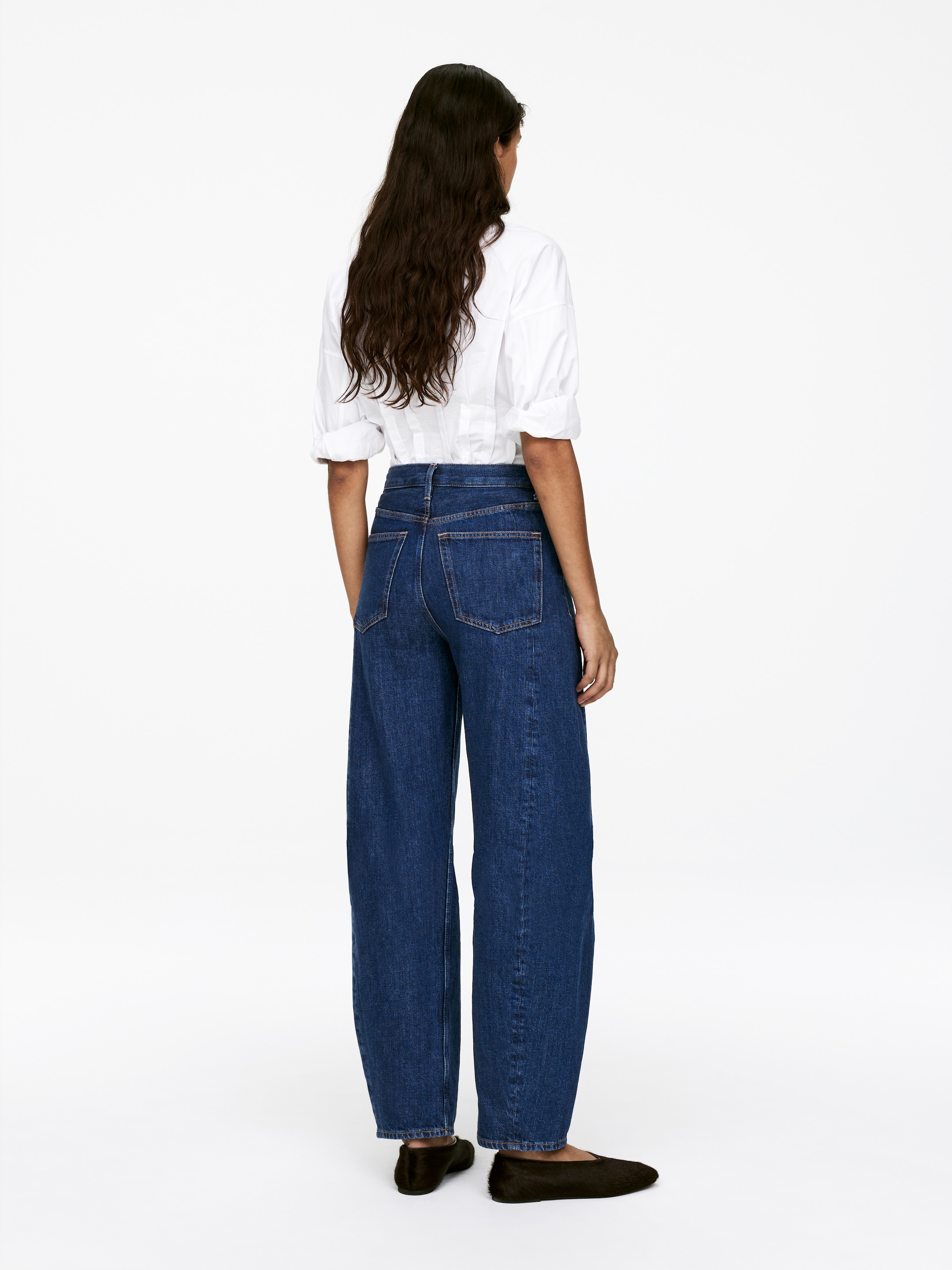 View larger image: Dark blue wide-leg jeans are being presented from the back, featuring a high waist and two visible back pockets. Their full-length legs are pooling slightly over dark flats, while a white shirt is being tucked into the waistband, highlighting the jeans' high-rise design.