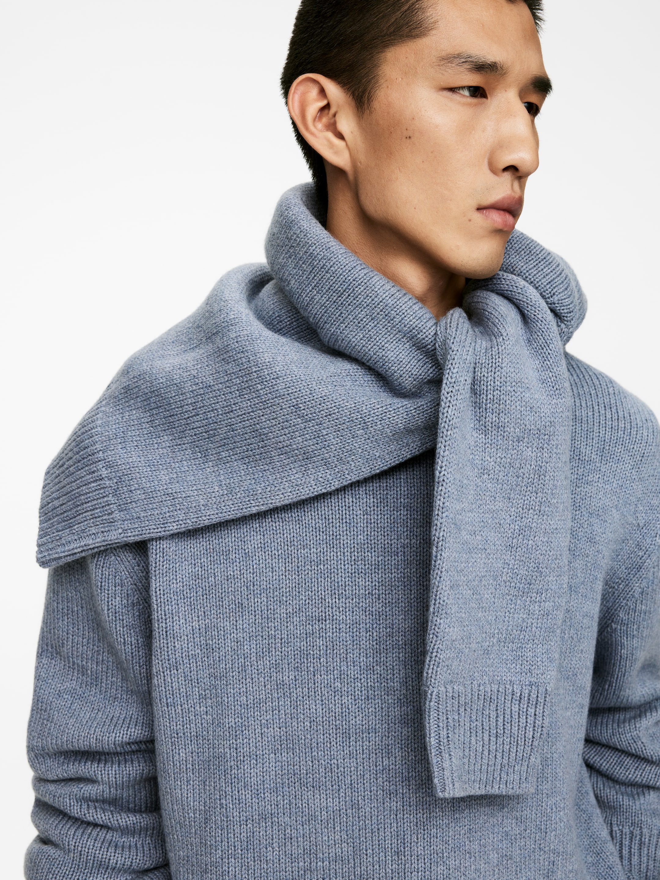 Größeres Bild anzeigen: Ein hellblauer gestrickter Pullover wird gezeigt, der eine gerippte Manschette am rechten Ärmel aufweist. Ein passender gestrickter Schal wird um den Hals drapiert, wobei ein Ende vorne herunterhängt und ein geripptes Finish zeigt.