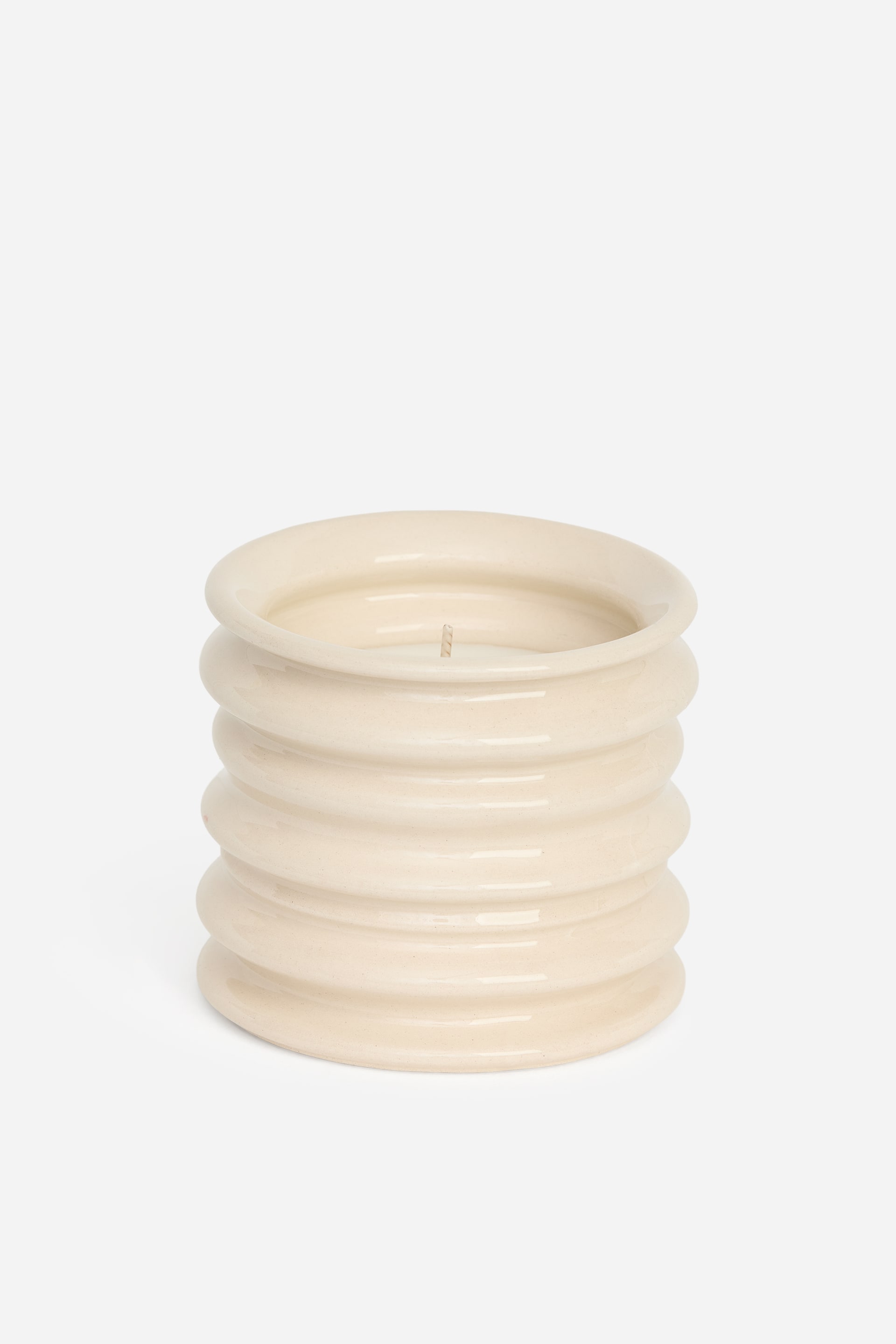 Ver imagem maior: Uma vela perfumada repousa dentro de um recipiente de faiança com acabamento brilhante e cor creme, apresentando saliências horizontais empilhadas. A vela de pavio único está visível no interior do recipiente cilíndrico, que exibe um rebordo superior ligeiramente alargado.