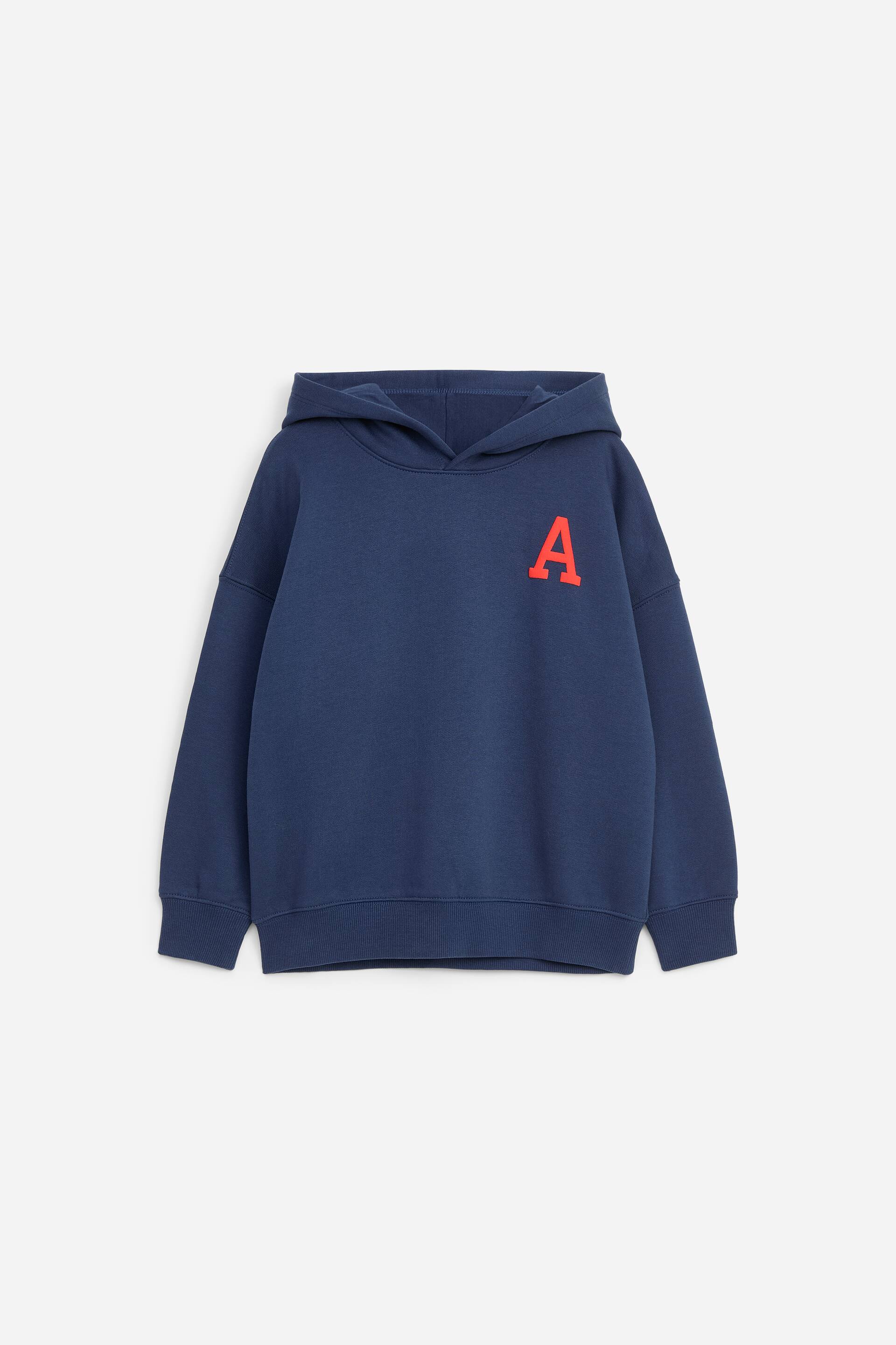 Visualizza immagine più grande: Una felpa con cappuccio blu navy è mostrata frontalmente, con una lettera "A" rossa stampata sul lato sinistro del petto. Il capo presenta spalle scese, maniche lunghe con polsini a coste e fondo a coste.