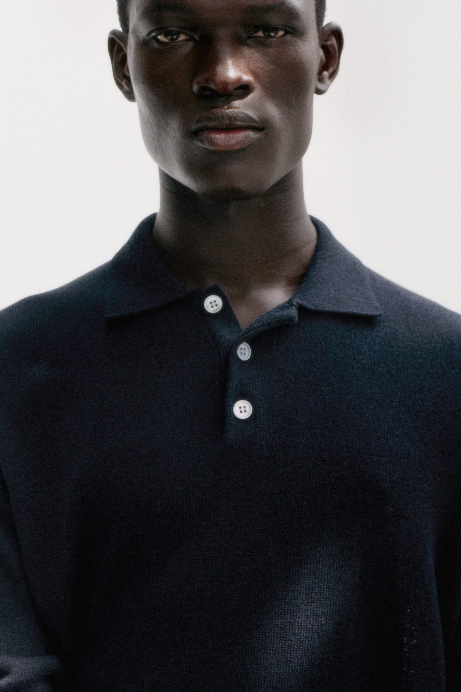 Grösseres Bild ansehen: Ein dunkelblaues Strick-Poloshirt mit klassischem Kentkragen und einer Drei-Knopf-Leiste, gesichert durch drei hellfarbige Knöpfe.