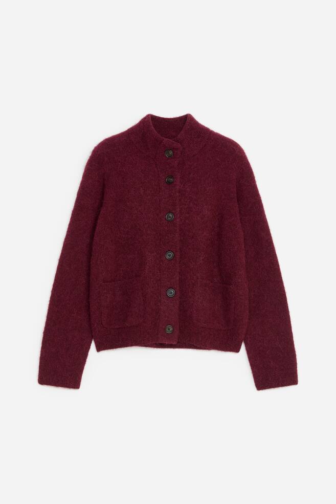 A burgundy knit cardigan is facing front, showcasing a fuzzy, plush texture and a relaxed fit. The cardigan features a high mock collar, a button-down placket with dark buttons, and two front patch pockets. - 1