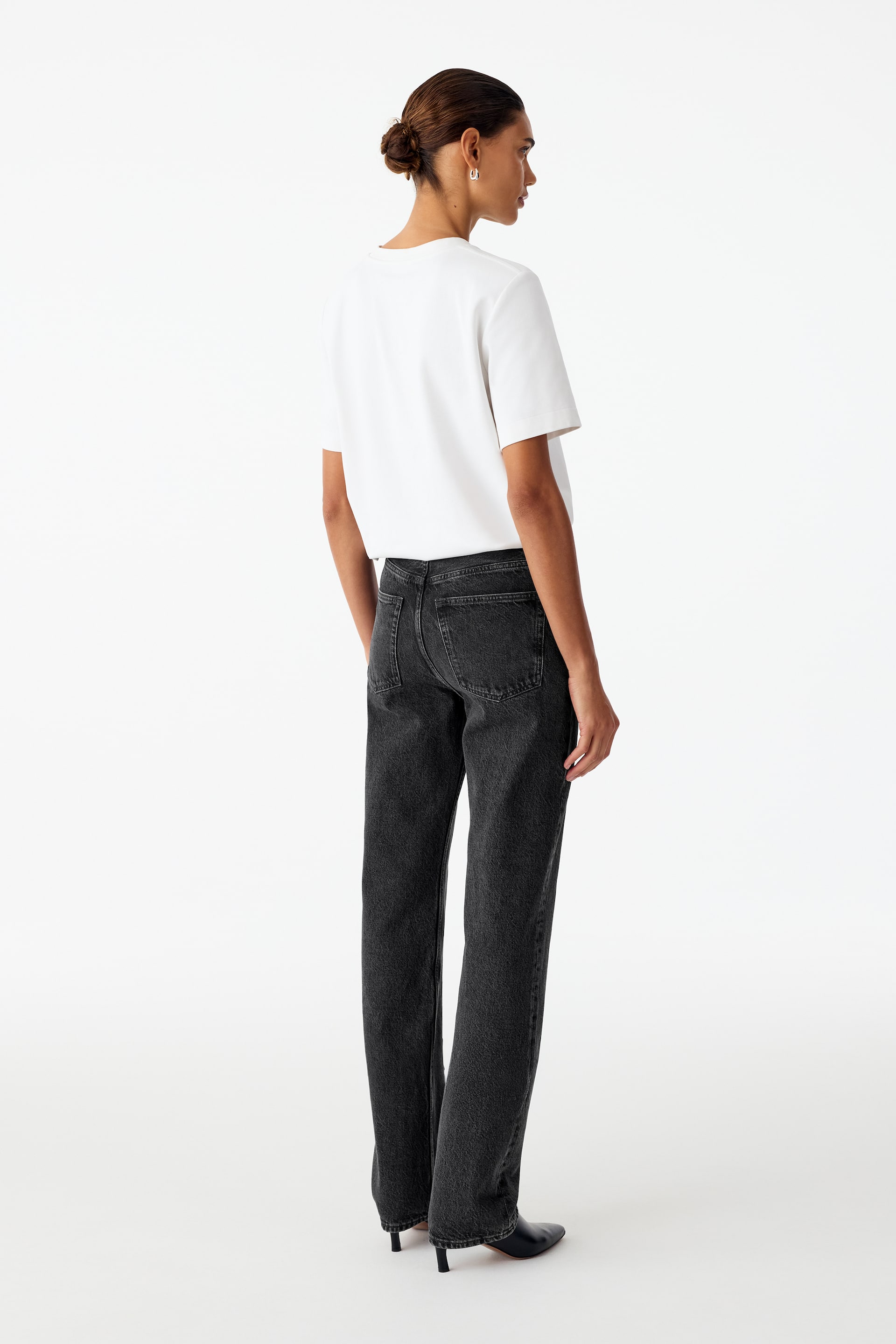 Visa större bild: Mörkgråa jeans med raka ben bärs av modellen och visar en medelhög midja samt klassiska bakfickdetaljer från ett bakifrån-vinklat perspektiv. Jeansen är stylade med en instoppad vit t-shirt och svarta boots med klack.