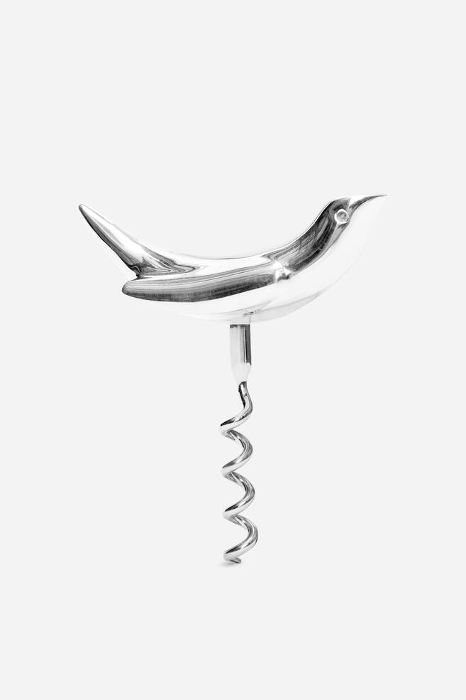 A polished metal corkscrew features a sleek, bird-shaped handle with a pointed beak and tail, and a spiral worm extending downwards from its belly. - 1