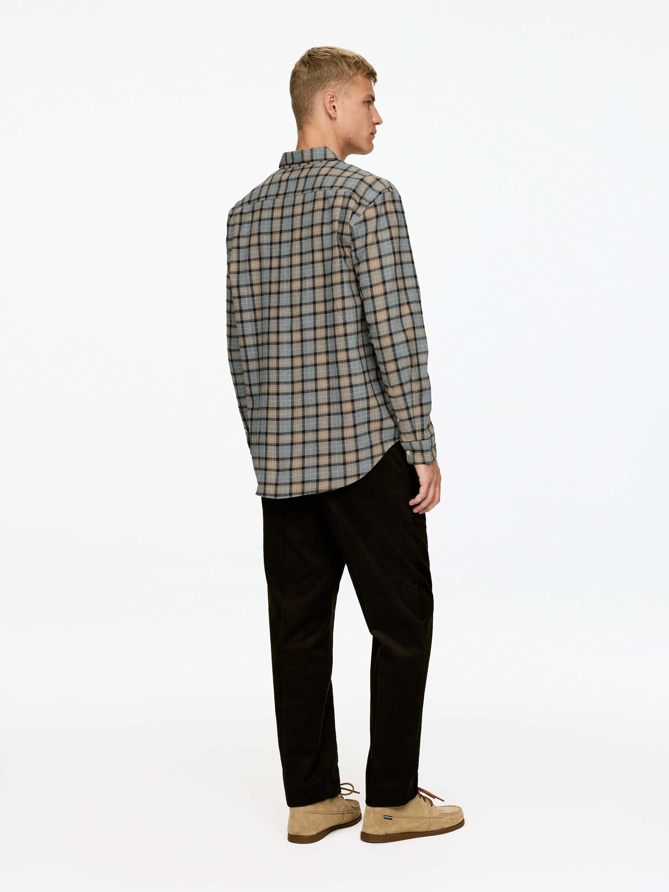 Ver imagen más grande: Una camisa de cuadros de manga larga en gris, beige y negro se lleva puesta, combinada con pantalones de pana marrón oscuro y zapatos de ante beige con cordones, todo visto desde un ángulo trasero-lateral.
