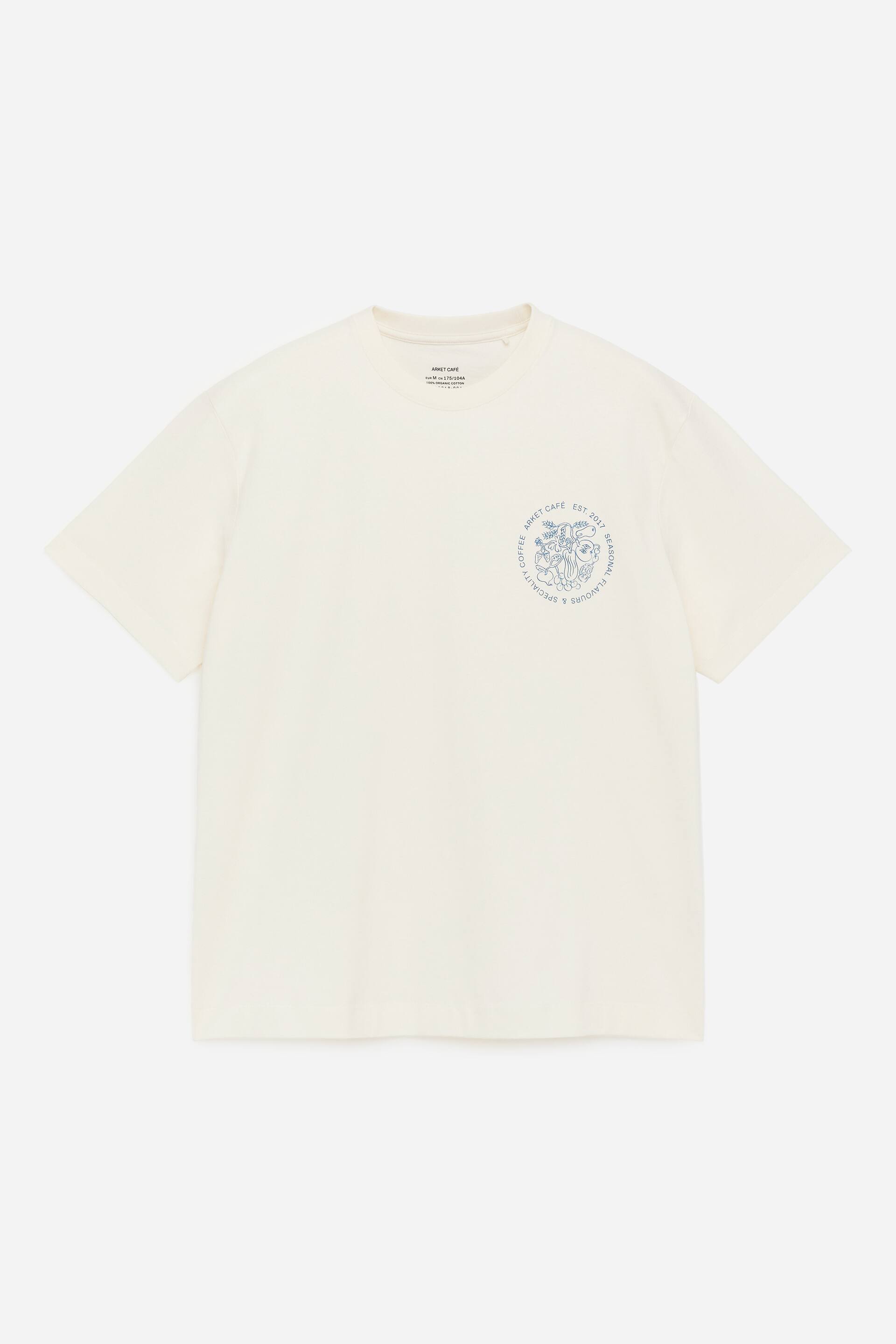 Agrandir l'image: Un t-shirt blanc cassé est présenté de FACE, avec un col rond et des manches courtes. Un imprimé graphique circulaire bleu orne la poitrine avant, affichant des illustrations complexes et du texte, y compris "ARMET CAFE EST. 2017 SAVEURS SAISONNIÈRES & CAFÉ SPÉCIALITÉ."