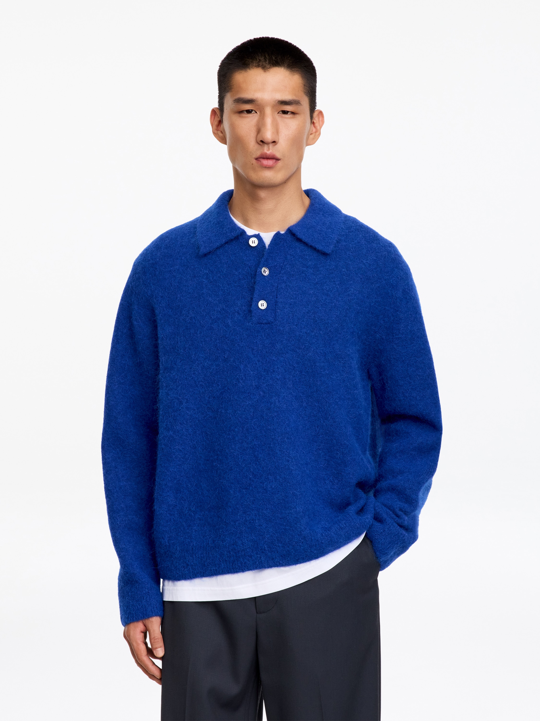 Un maglione polo in maglia blu royal Ã¨ mostrato frontalmente, con una finitura soffice e testurizzata e una vestibilitÃ  rilassata. Il maglione presenta un classico colletto polo con abbottonatura a tre bottoni, maniche lunghe e orlo dritto.
