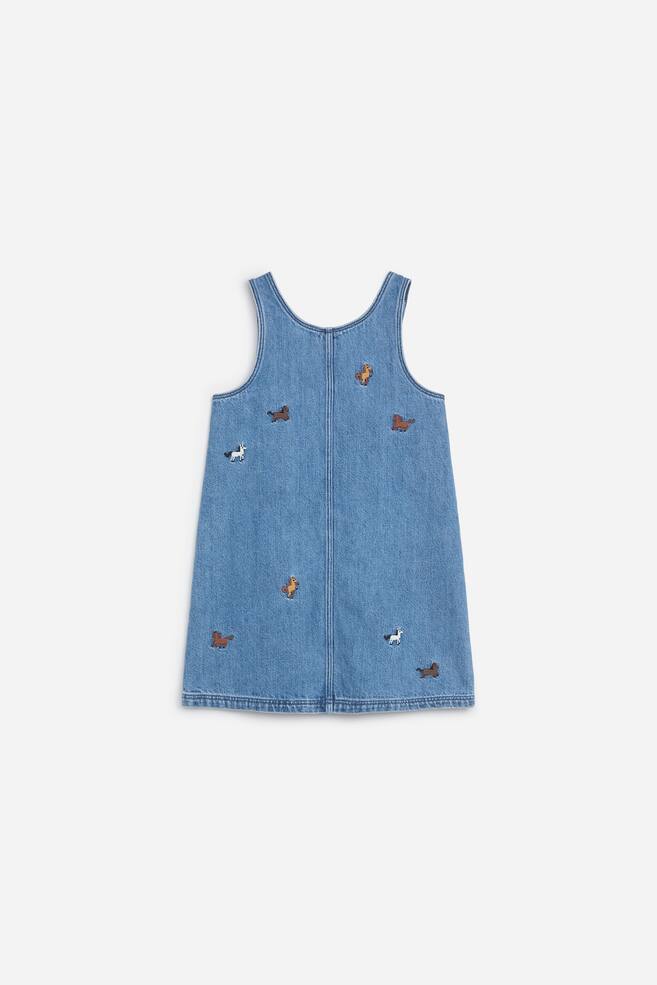 Ein blaues Denim-SchÃ¼rzenkleid ist von hinten zu sehen und zeigt eine leichte A-Linien-Silhouette mit einer vertikalen Mittelnaht. Es ist mit kleinen, verstreuten gestickten Pferdemotiven in WeiÃ, Braun und Beige auf dem mittelschwer gewaschenen Stoff versehen. - 1