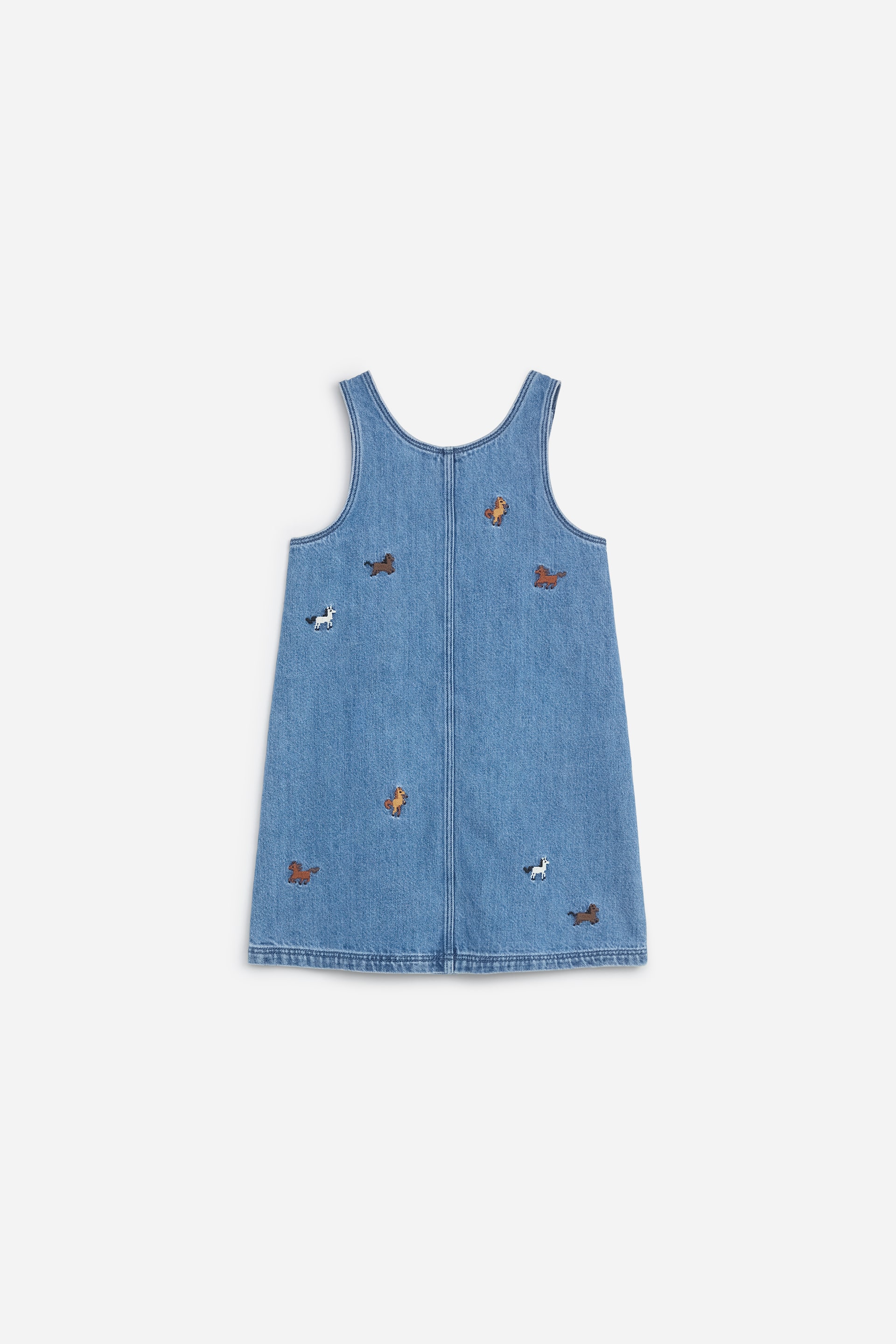 Vis større bilde: En blå denimforklekjole er vist bakfra, med en lett A-linjeform og en vertikal søm i midten. Den har små, spredte broderte hestemotiver i hvitt, brunt og tan over det mediumvaskede stoffet.