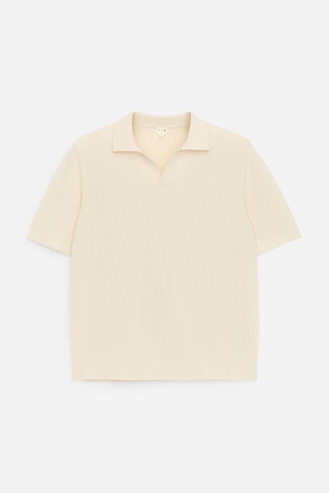 A light cream polo shirt is showcasing its front view, featuring a textured knit surface. It is designed with short sleeves and a V-neck spread collar, maintaining a regular fit. - 1