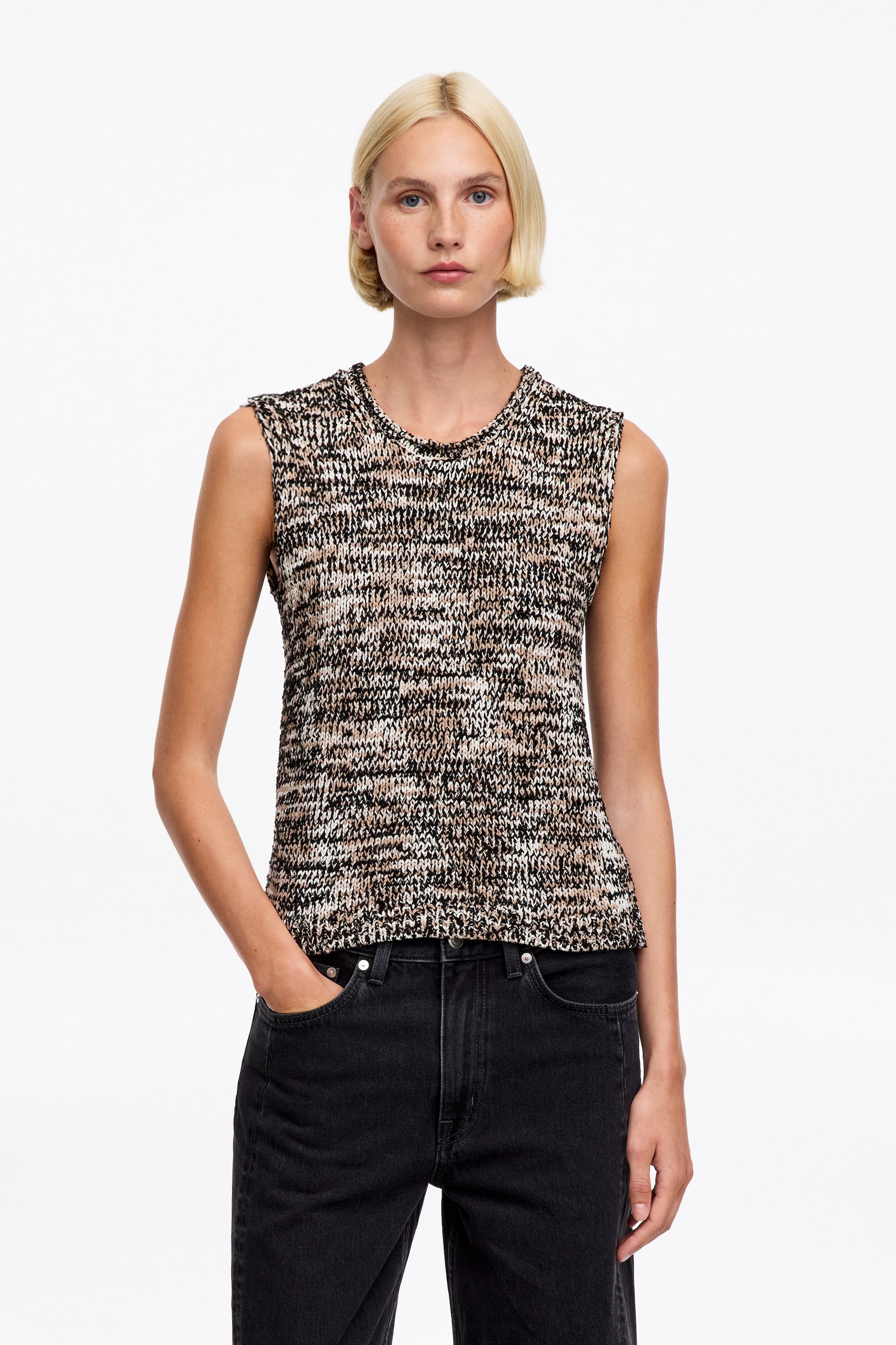 Visualizza immagine più grande: Il top in maglia senza maniche, caratterizzato da scollo rotondo e motivo mélange nei toni del nero, bianco e beige, è indossato dalla modella e abbinato a jeans neri.