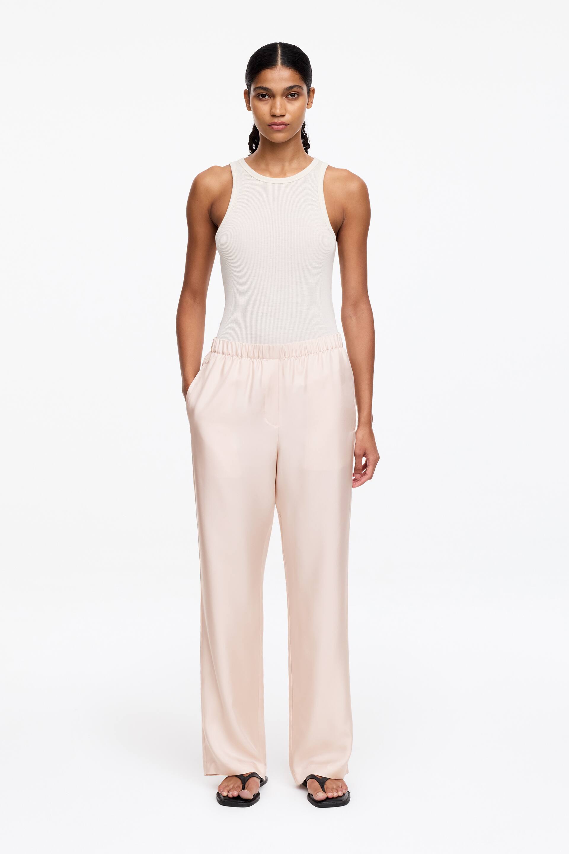 Grösseres Bild ansehen: Seidentwill-Hosen mit elastischem Bund und Paspeltaschen an den Seitennähten werden vom Model getragen. Das Model steht und hat eine Hand in eine Seitentasche der Hose gesteckt.