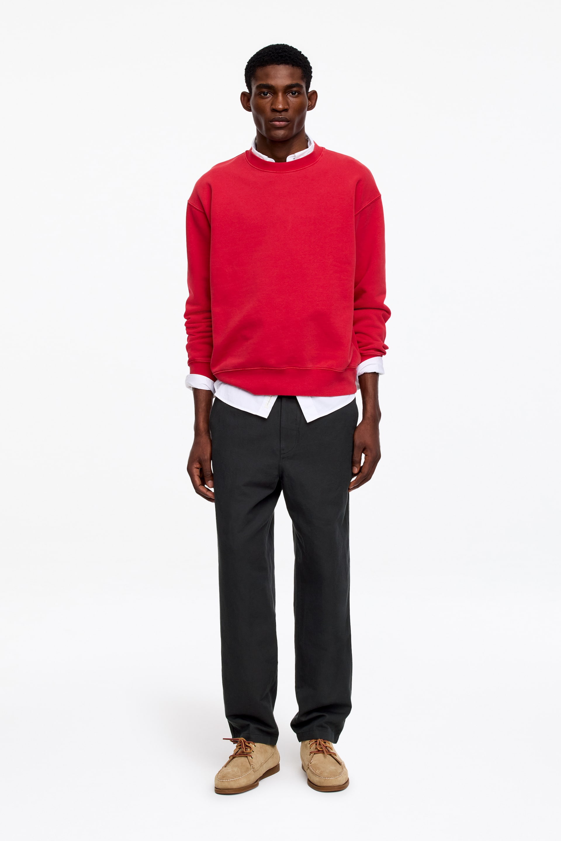 Se større billede: En rød crew neck sweatshirt viser lange ærmer med ribbede manchetter og en ribbet kant. Den bæres over en hvid skjorte med krave, hvor skjortens krave og manchetter stikker ud under sweatshirten.