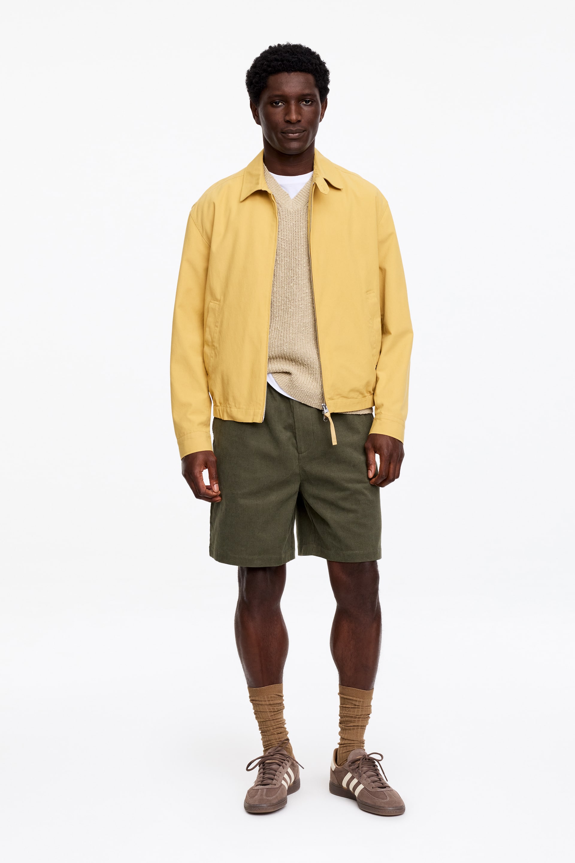 Visualizza immagine più grande: "Una giacca gialla presenta un colletto a punta, una chiusura frontale con zip completa e tasche laterali. È inoltre dotata di polsini con bottoni e un orlo dritto, stratificata su un maglione beige chiaro con scollo a V."