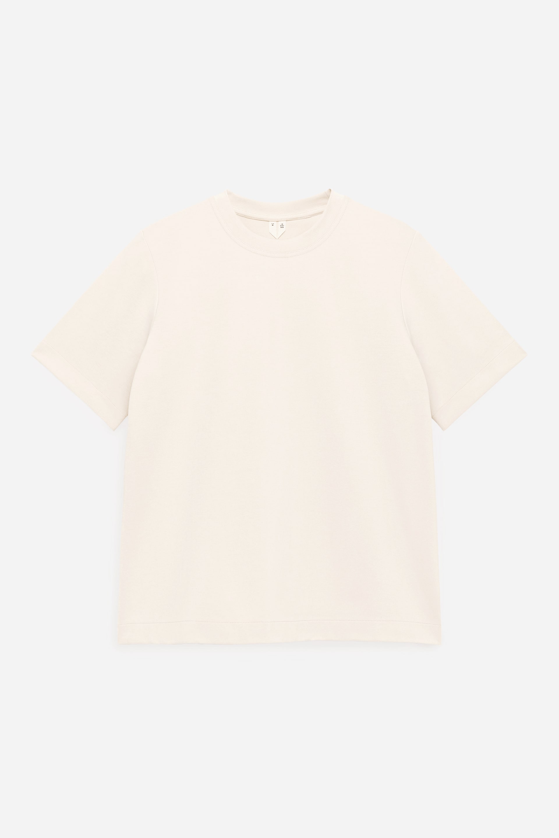 Grotere afbeelding bekijken: Een crèmekleurig T-shirt is van voren weergegeven, met een klassieke ronde hals en korte, losvallende mouwen. Het kledingstuk ligt plat, waardoor het regular-fit silhouet en de strakke, minimalistische stiksels bij de zoom en manchetten goed zichtbaar zijn.