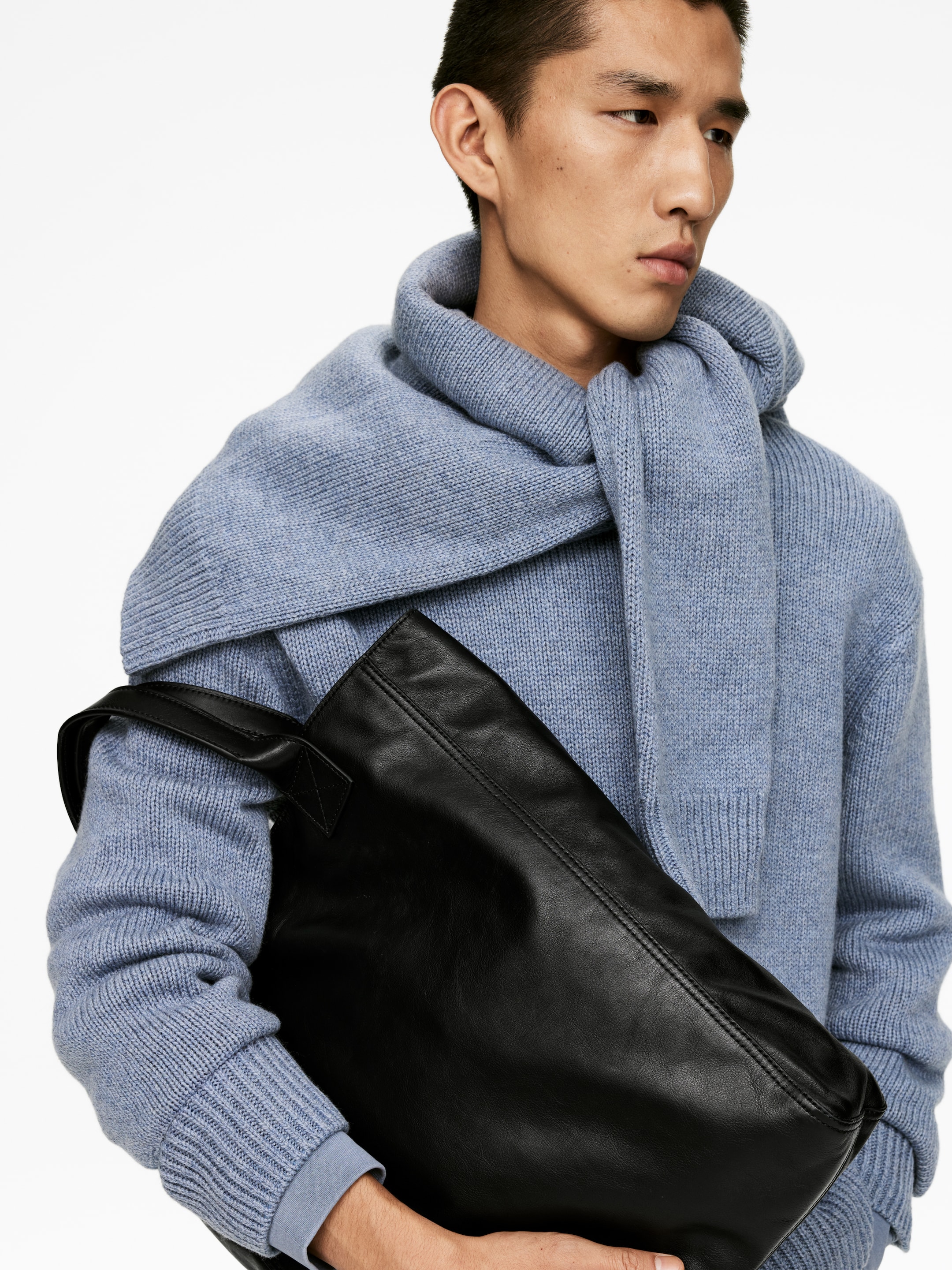 Größeres Bild ansehen: Eine schwarze Ledertasche wird schräg über den Oberkörper einer Person getragen. Sie hat eine glatte Textur, eine sichtbare Naht, die horizontal über den oberen Bereich verläuft, und einen flachen Tragegriff an der Oberseite.