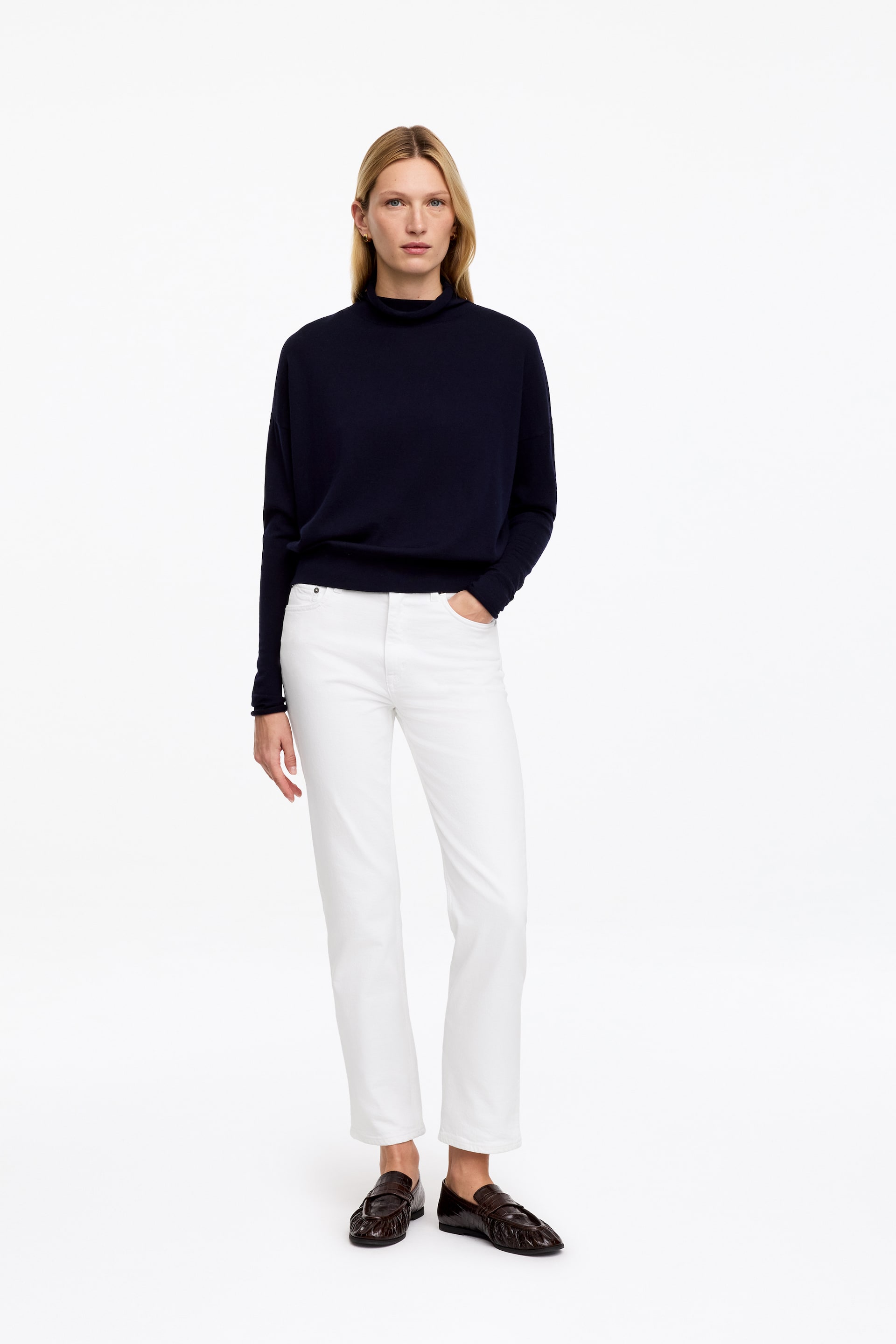 Agrandir l'image: Le mannequin porte un jean JADE CROPPED blanc, à taille mi-haute, à silhouette ajustée et à jambe fuselée raccourcie. Le mannequin porte également un pull à col roulé foncé et des mocassins foncés.