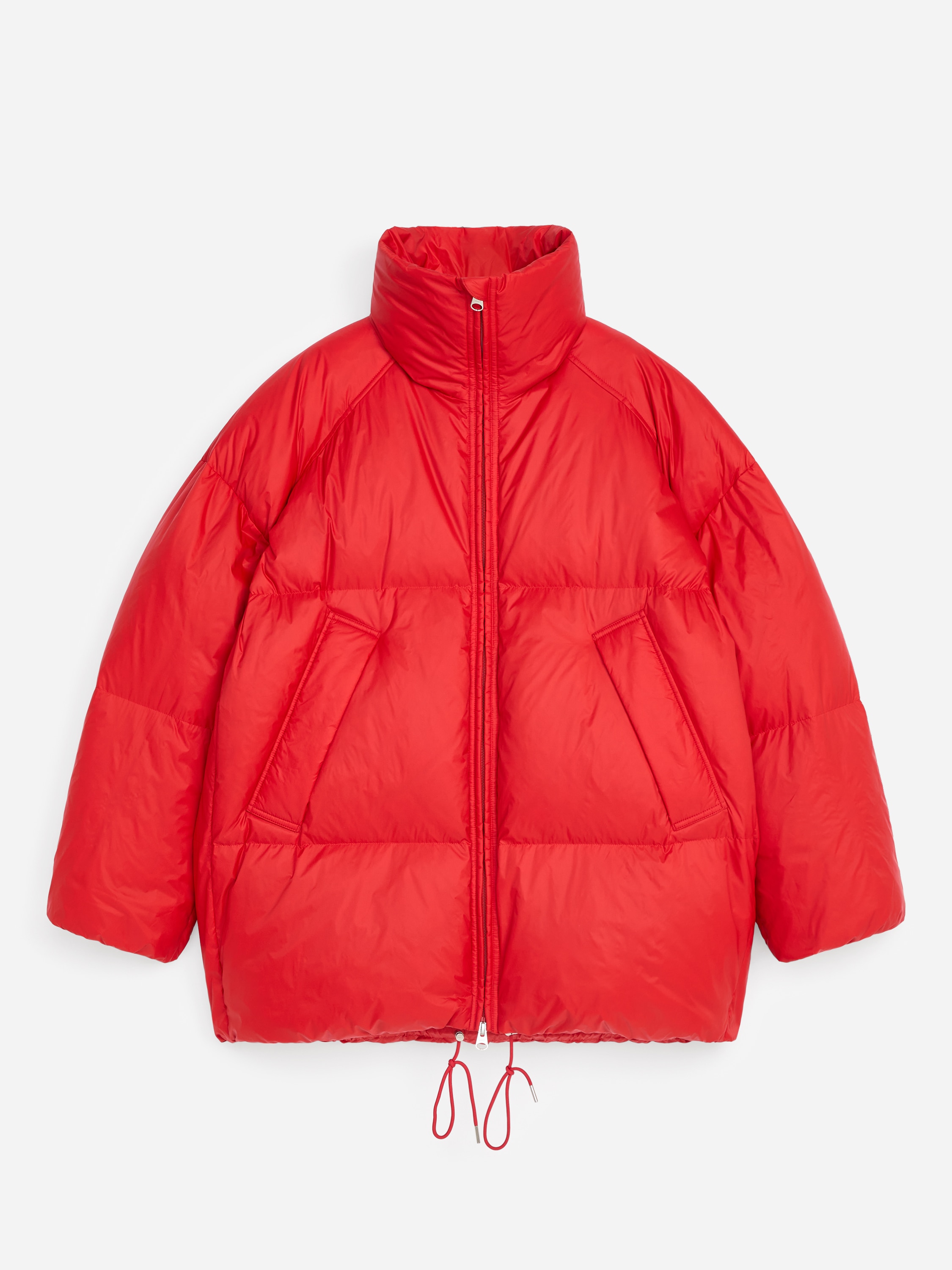 Eine leuchtend rote Steppjacke wird von vorn getragen und zeichnet sich durch ein voluminöses, gestepptes Design mit einem breiten, hohen Kragen und einem Reißverschluss vorne aus. Die Jacke wird über einem farblich passenden, roten, strukturierten Strickkragen getragen, während die Person die Arme verschränkt, um die voluminöse Struktur der Ärmel zu betonen.