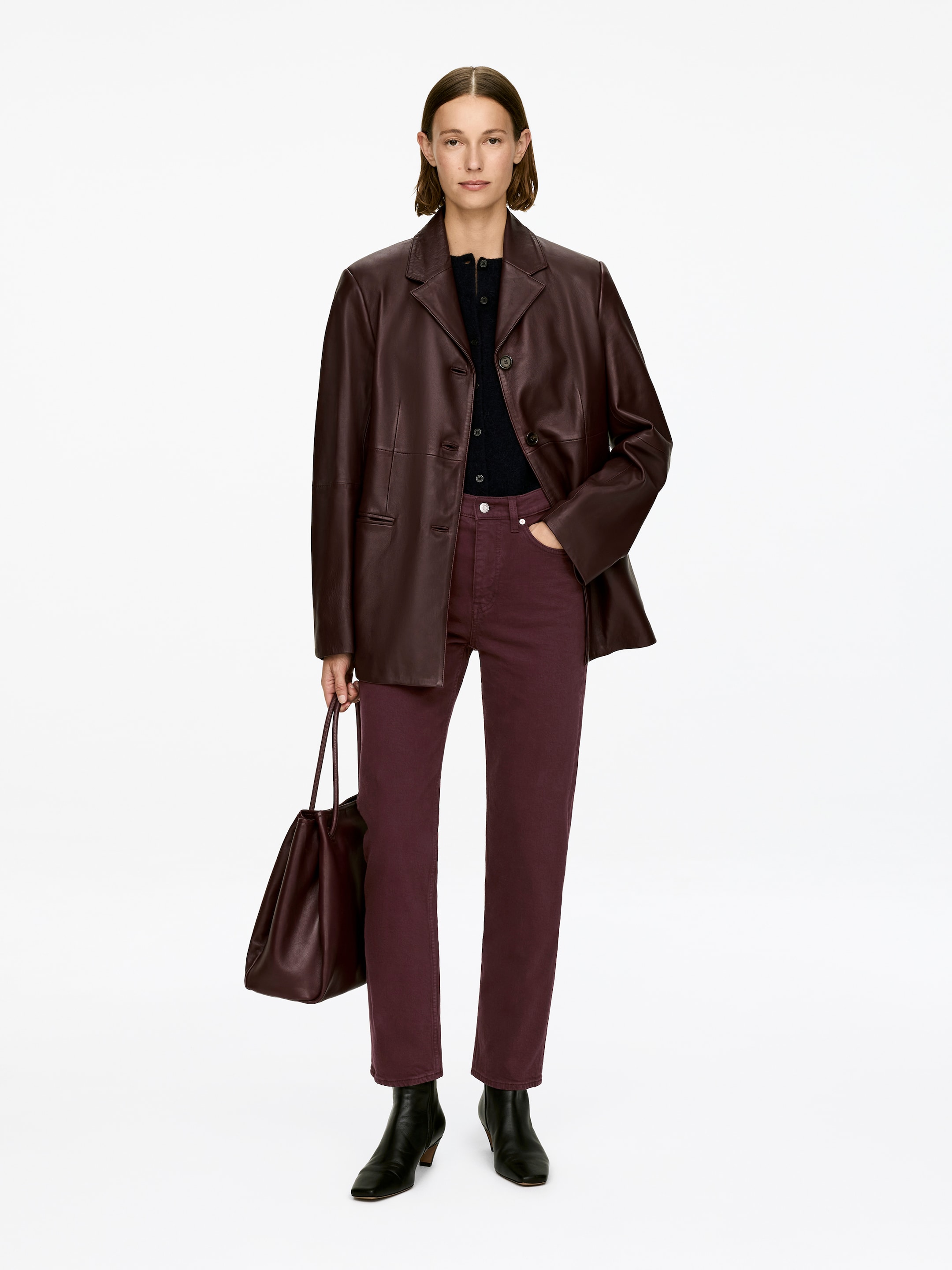 View larger image: JADE CROPPED jeans are a dark red hue with a mid-rise waist, slim fit, and tapered, cropped legs. The model is wearing the jeans, with one hand resting in a front pocket, and the cropped length is revealing black ankle boots.