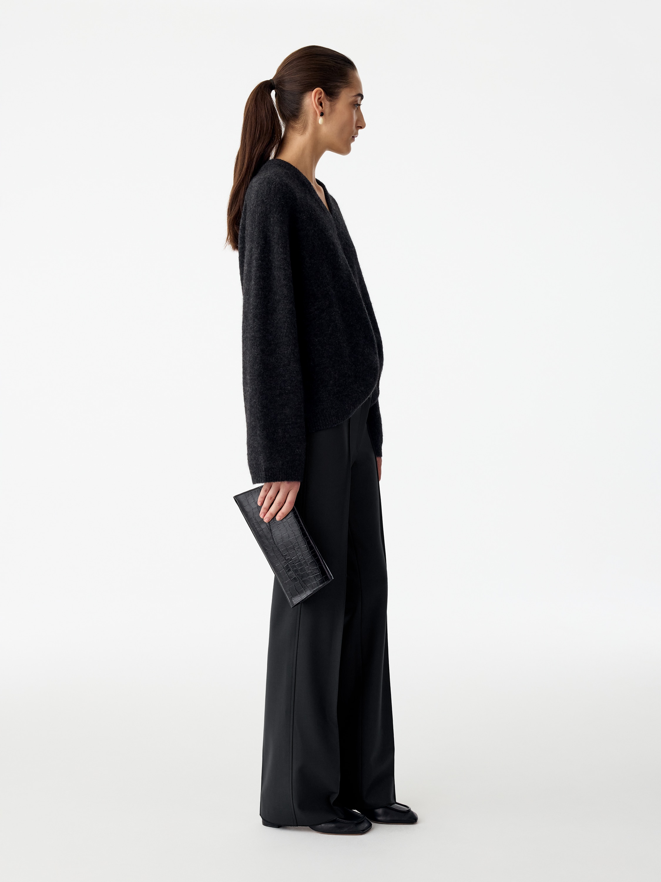 A pair of slim-fitting tailored trousers in black is shown from the front, featuring a low-rise waist with belt loops and a flared leg. Sharp, sewn-in creases run vertically down the centre of each leg.