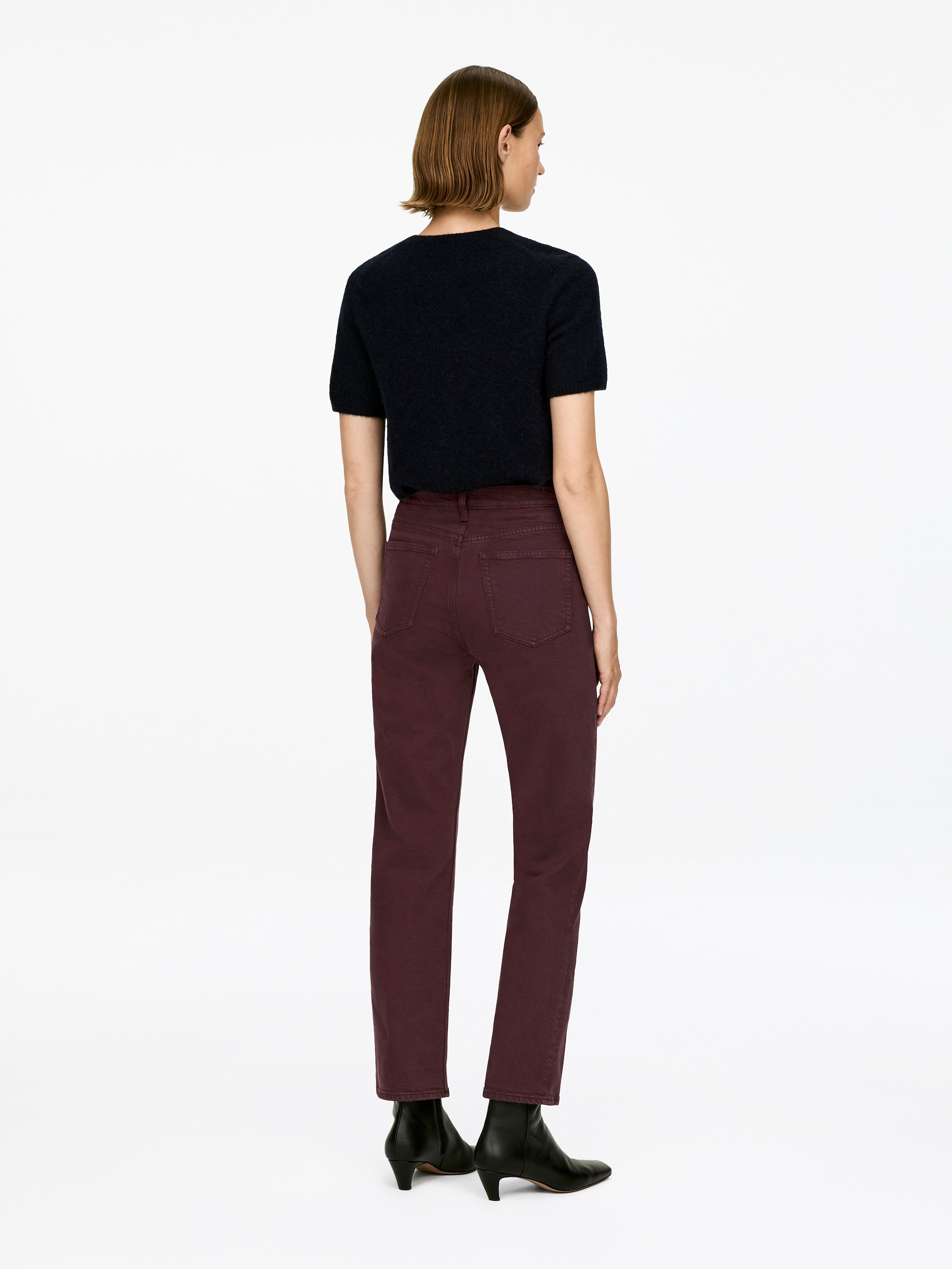 View larger image: The dark red JADE CROPPED pants are being worn by the model, showing a mid-rise waist, slim fit, and tapered, cropped legs. The pants are falling just above black ankle boots, emphasizing their length.
