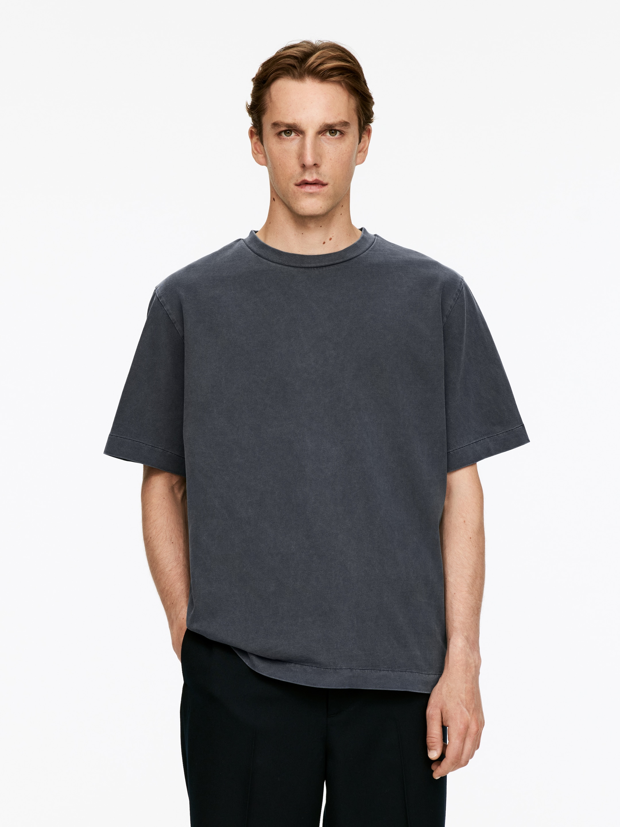 Ver imagen más grande: Una camiseta gris oscuro se presenta en una vista frontal. Presenta un cuello redondo y mangas cortas, mostrando un ajuste holgado y un acabado desgastado.