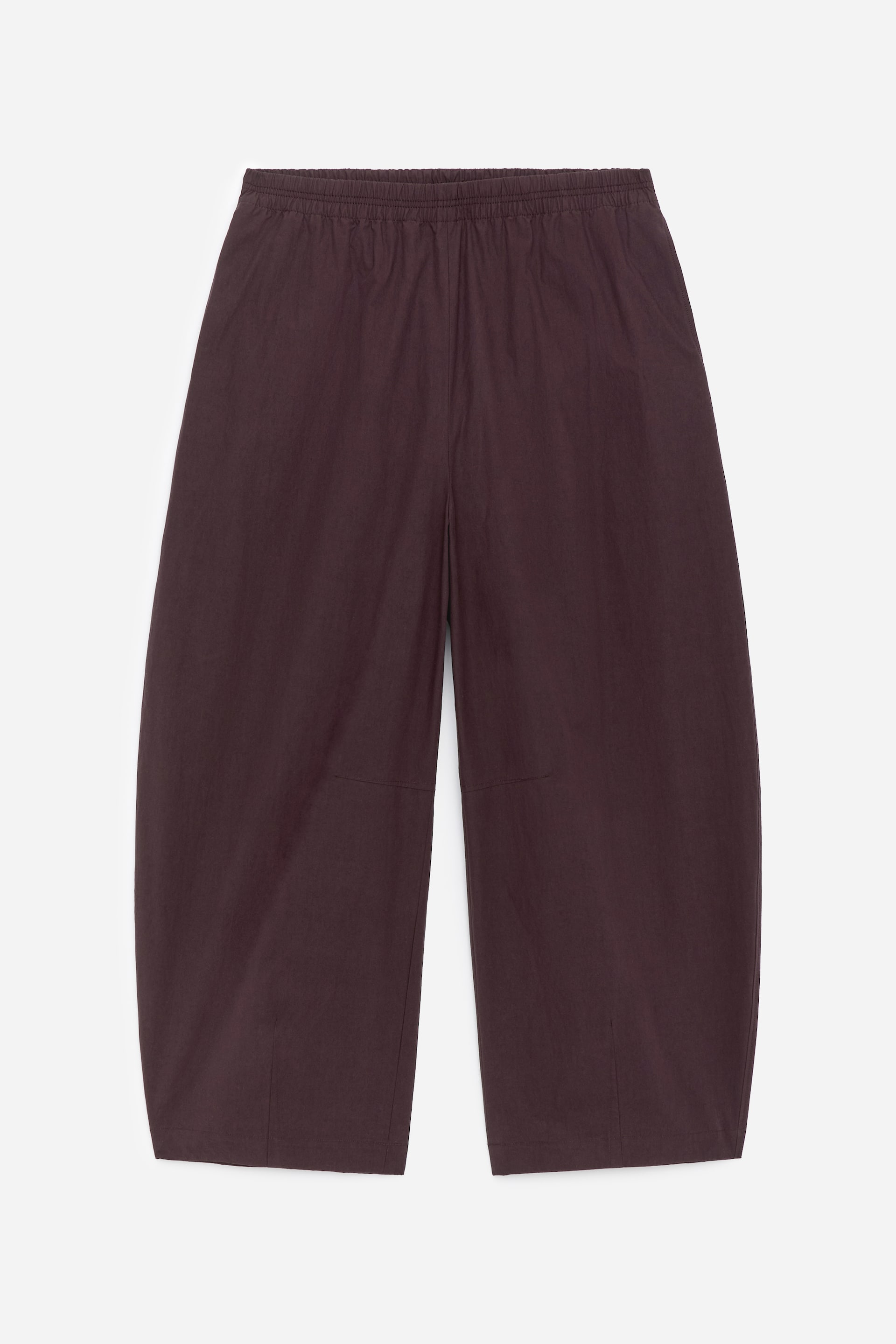 Ver imagen más grande: Un par de pantalones de color marrón oscuro se muestra desde el FRENTE, con una cintura elástica y piernas anchas y cortas con una forma ligeramente curva. Se aprecian costuras horizontales justo por encima de las rodillas, y costuras verticales que recorren el centro frontal de cada pierna.