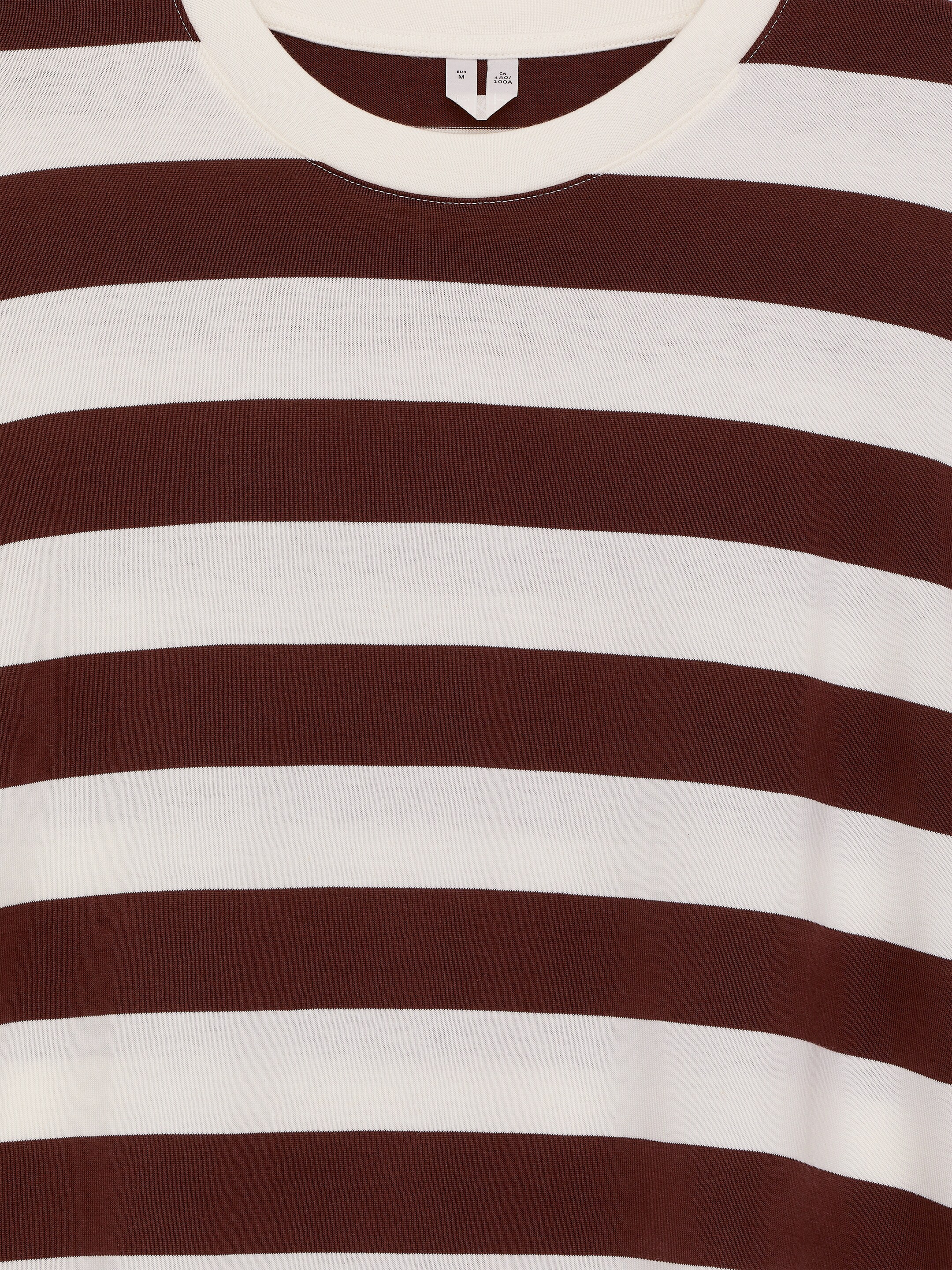 Agrandir l'image: Un T-shirt à manches longues est présenté de face, avec des rayures horizontales marron foncé et crème et un col rond crème. Une petite étiquette est visible à l'arrière du col.