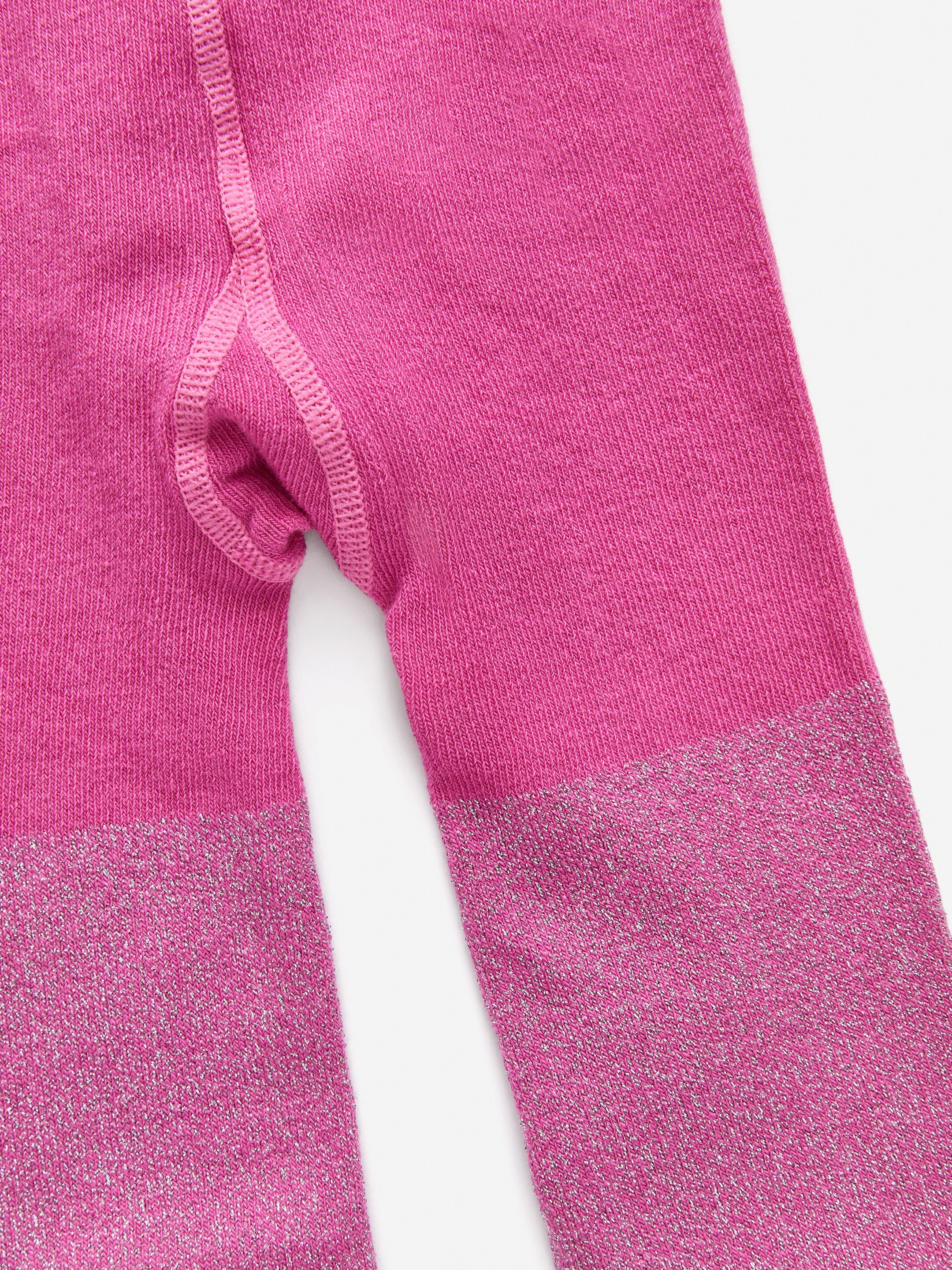 Grotere afbeelding bekijken: Gebreide panty's tonen een levendige magenta kleur met een fijne breistructuur. Het bovenste gedeelte vertoont een zichtbare kruisnaad, terwijl het onderbeen een zilveren metallic draad in het breisel heeft geweven, wat een opvallend glittereffect creëert.