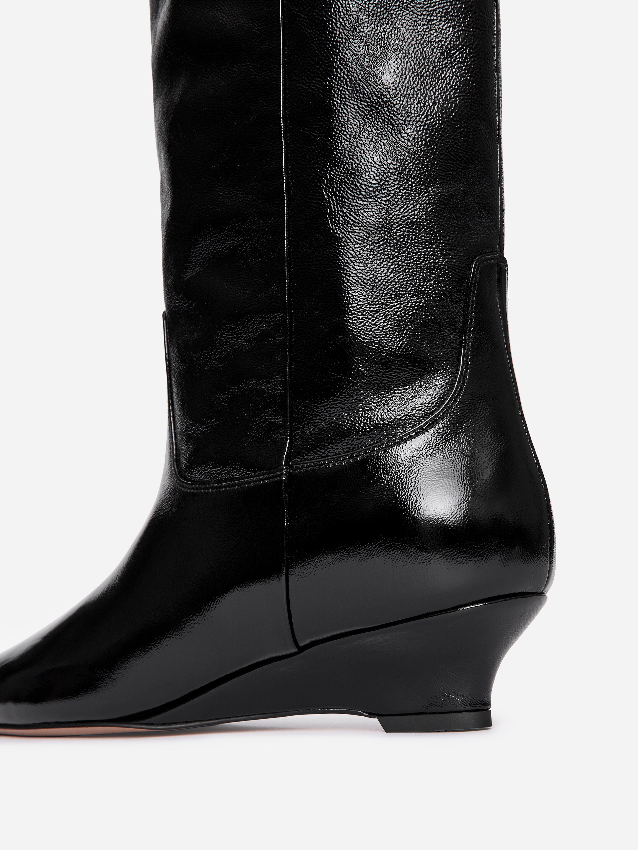 Agrandir l'image: Une botte en cuir noir brillant est orientée vers la droite, avec une tige haute, un bout pointu et un talon compensé noir.