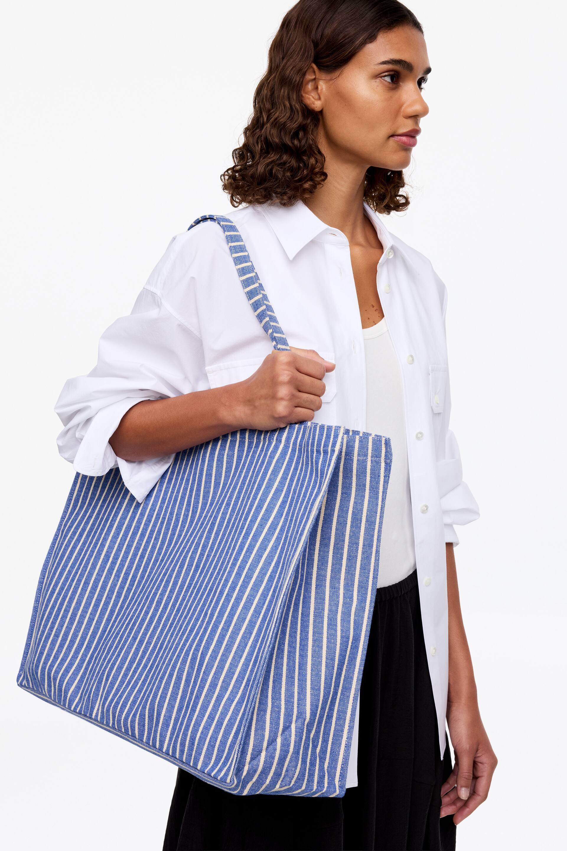 Ver imagen más grande: Una bolsa tote azul con rayas verticales blancas se lleva sobre el hombro, mostrando sus paneles frontal e inferior. La correa ancha, también a rayas, es visible.